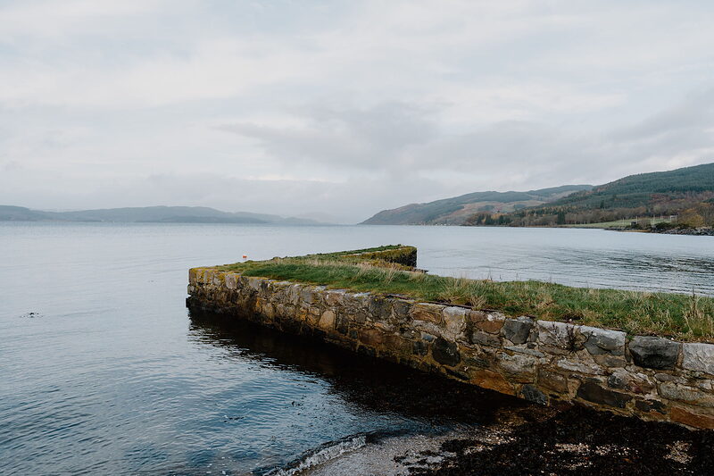 A stone pier reaching into a calm loch, hills lining the far shore.