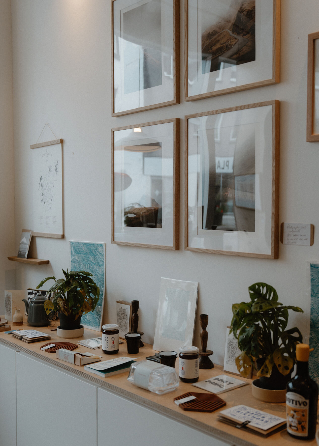 Inside The Modern Croft: framed prints on the wall above a long sideboard of candles, jars, plants and books.