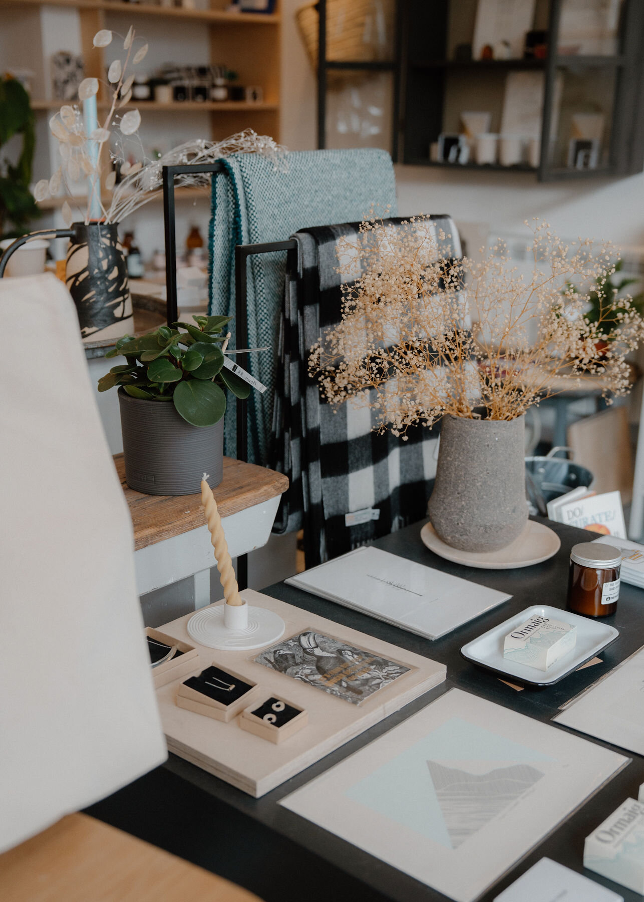 A table of homeware: a checked throw, dried gypsophila in a stone vase, candles and trinket dishes.