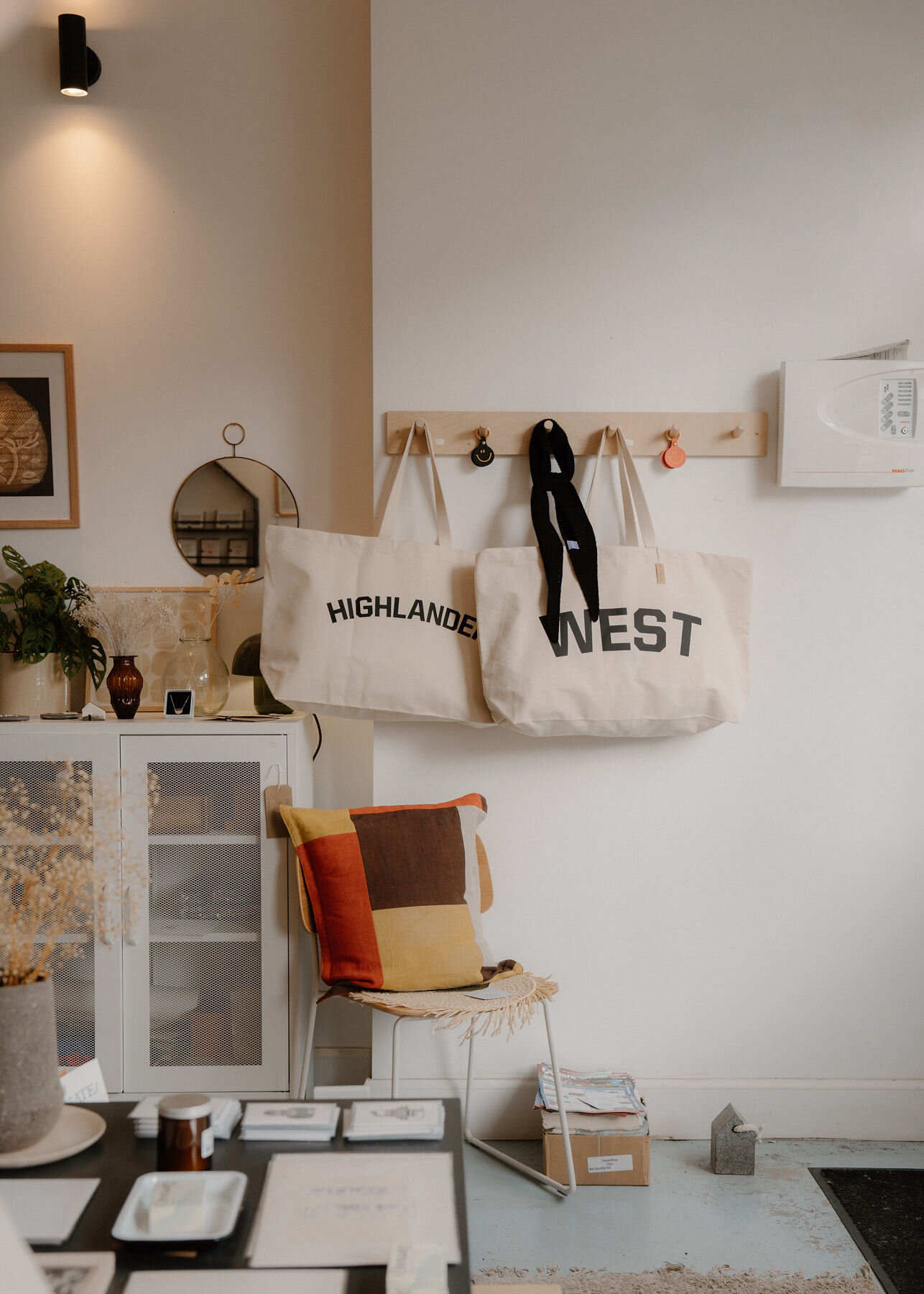 Highlander and West tote bags on pegs above a chair with a patchwork cushion in the shop.