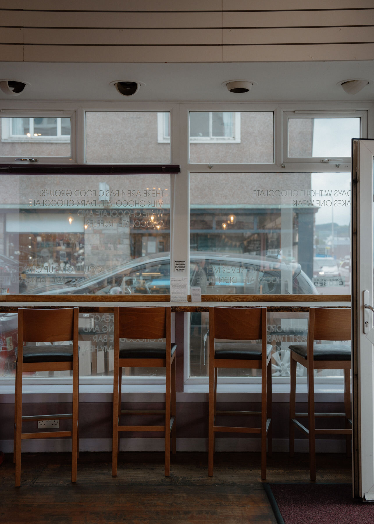 Tall stools along a window bar in the café, the street and the bay outside.