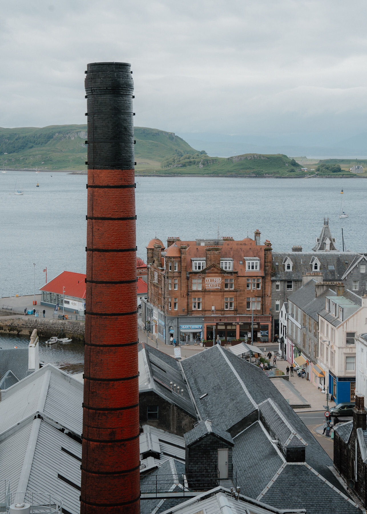 The distillery chimney beside the red sandstone Columba Hotel and the north pier, Kerrera across the bay.