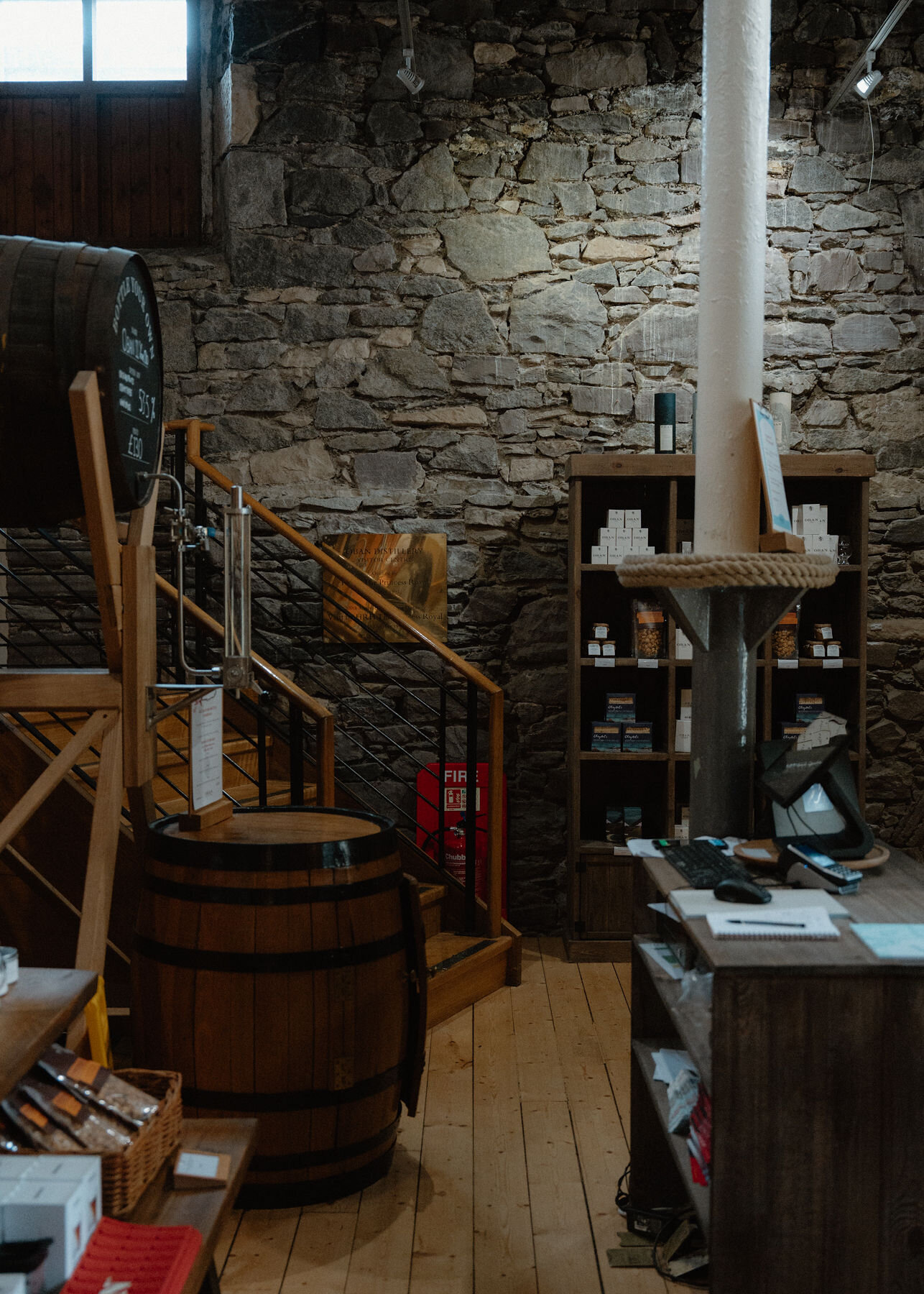 Inside the distillery shop: a cask, a timber staircase and shelves of bottles against a rough stone wall.