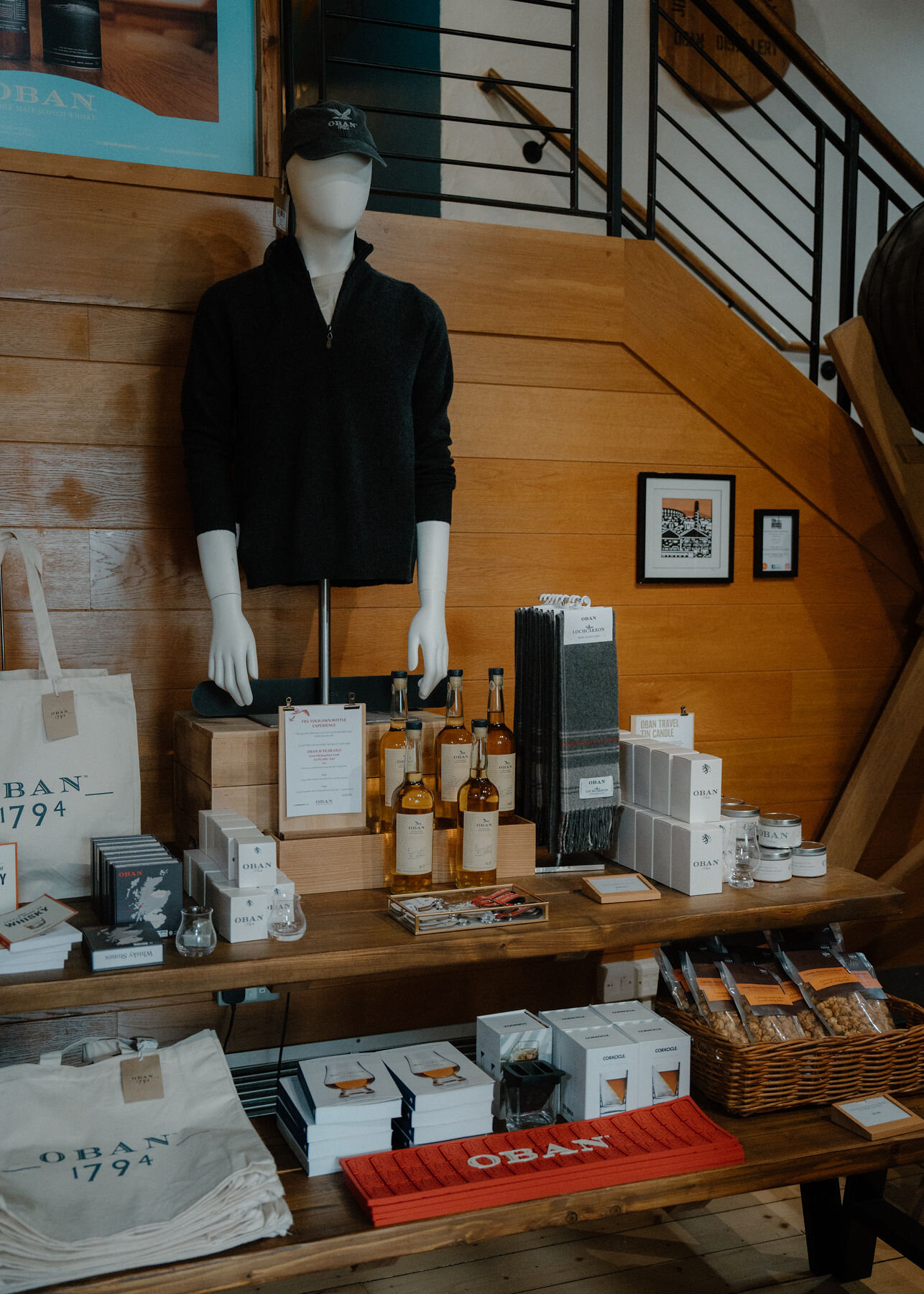 A mannequin in an Oban fleece above a table of whisky, gift boxes and tote bags in the distillery shop.