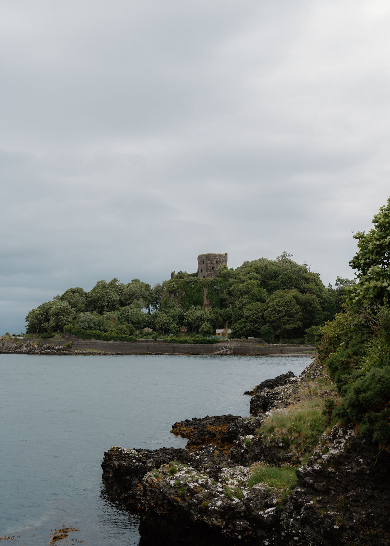 Rocks on the shore at the north end of the bay, Dunollie Castle on its wooded crag across the water.