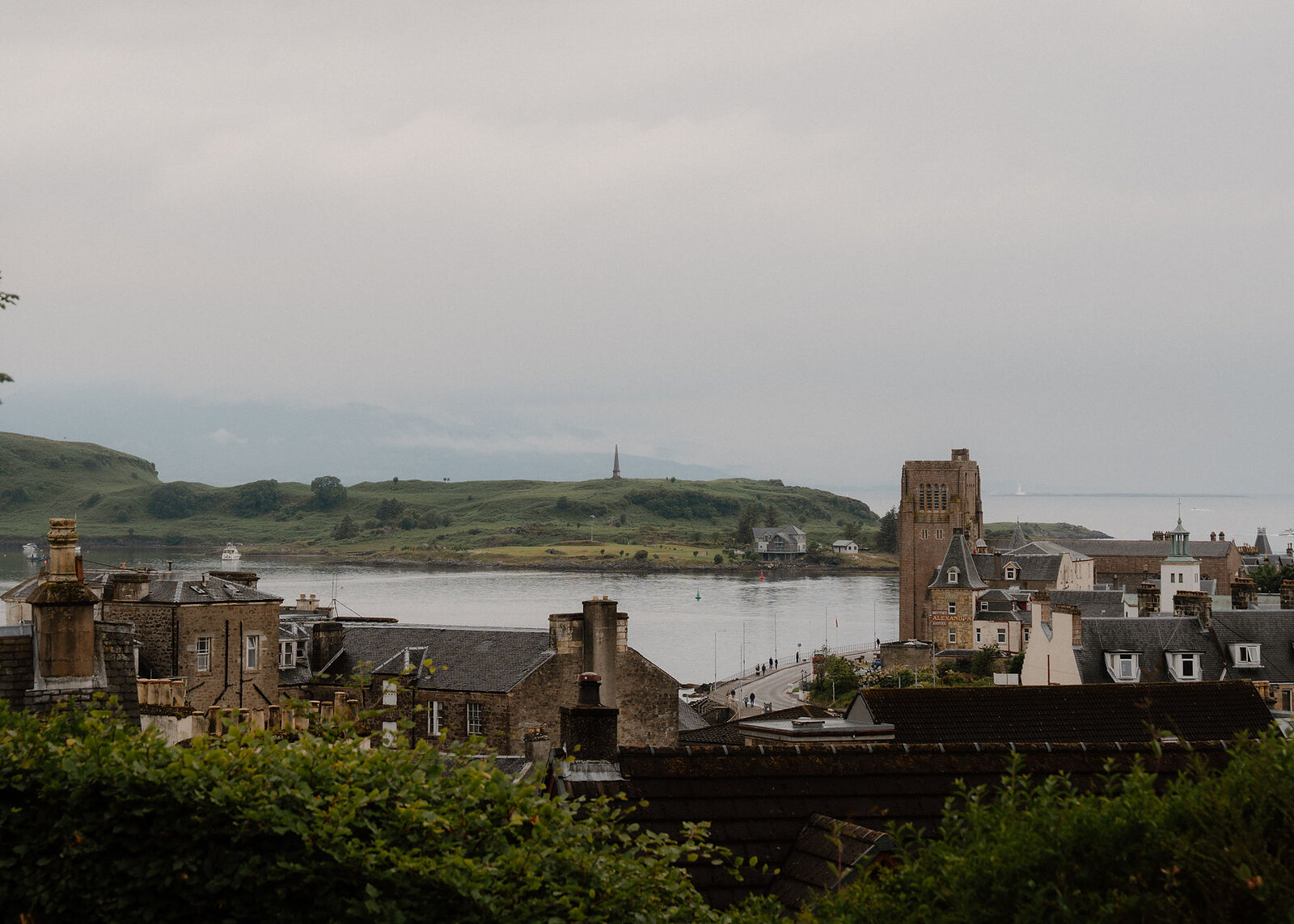 From the garden, Oban's slate roofs and chimneys fall to the bay, the square tower of St Columba's Cathedral on the shore and Kerrera beyond under grey cloud.