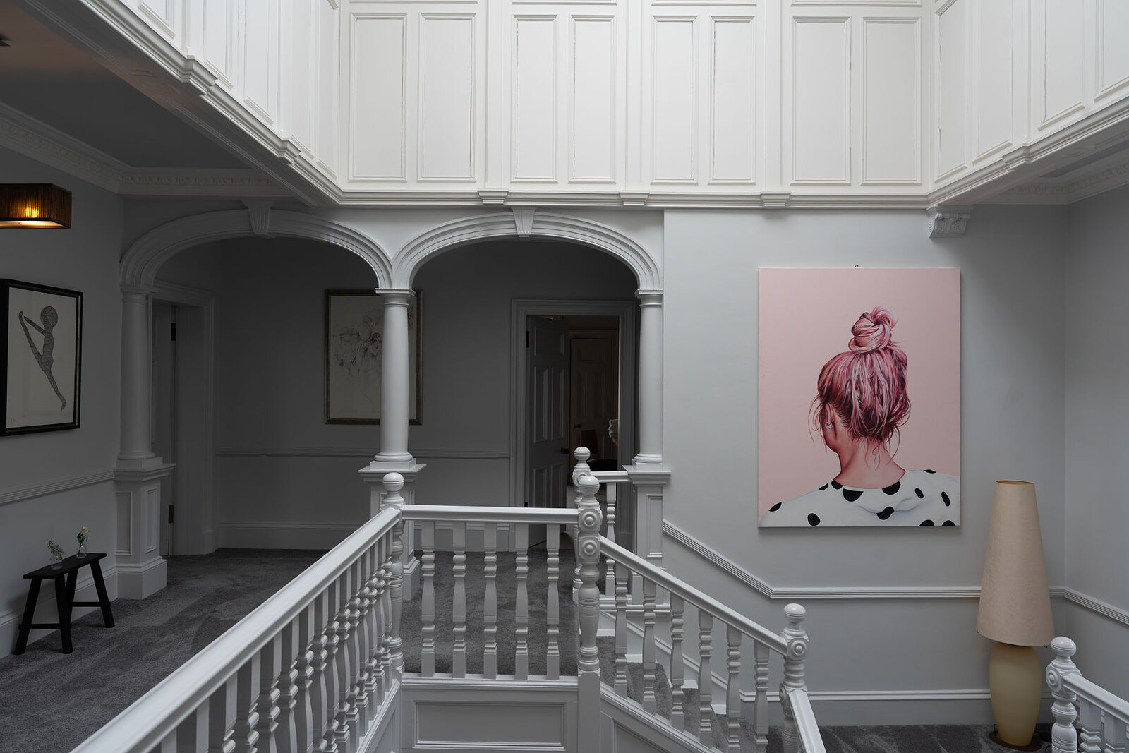 A landscape view of the galleried landing from the stairhead: arches on columns, doors round the gallery and the pink-haired portrait.