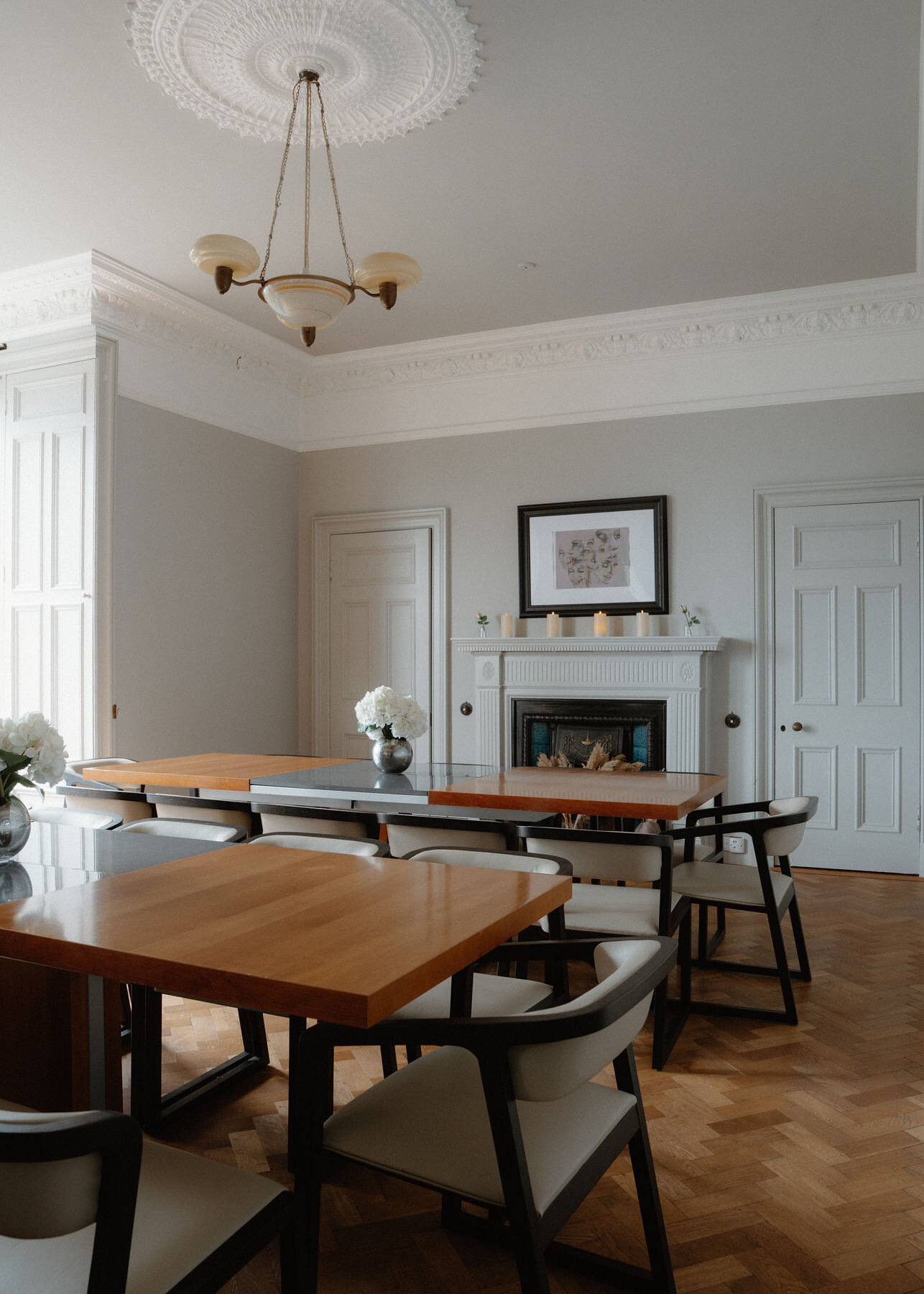 The dining room: long walnut and black glass tables with curved chairs on a herringbone floor, a fireplace under a brass pendant.