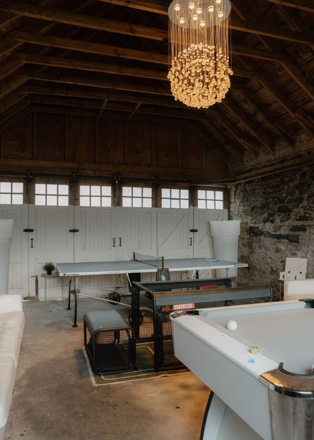 A crystal chandelier hangs from the timber roof of the games room over the table tennis table, the pool table and a row of small windows.