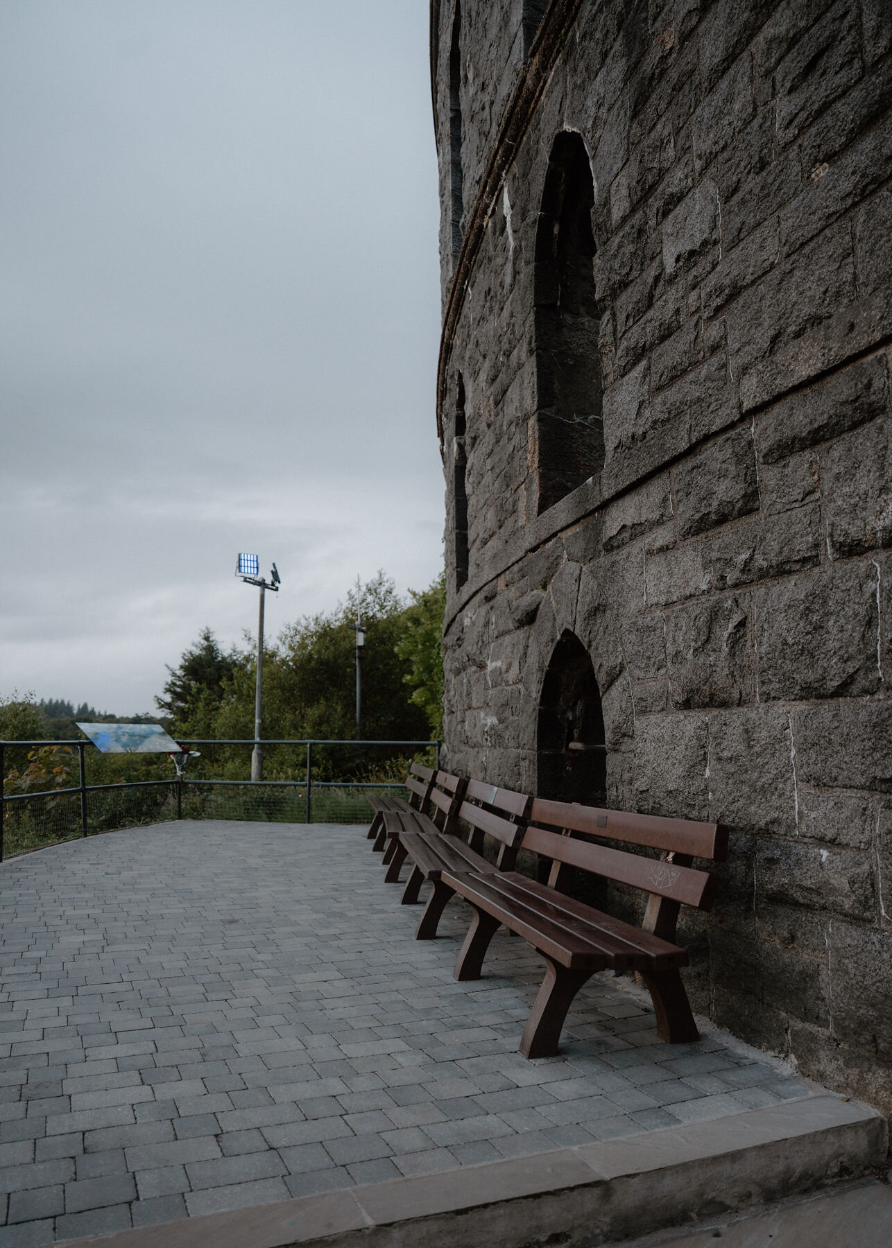 A bench against the rough granite wall of McCaig's Tower on the paved viewing terrace.