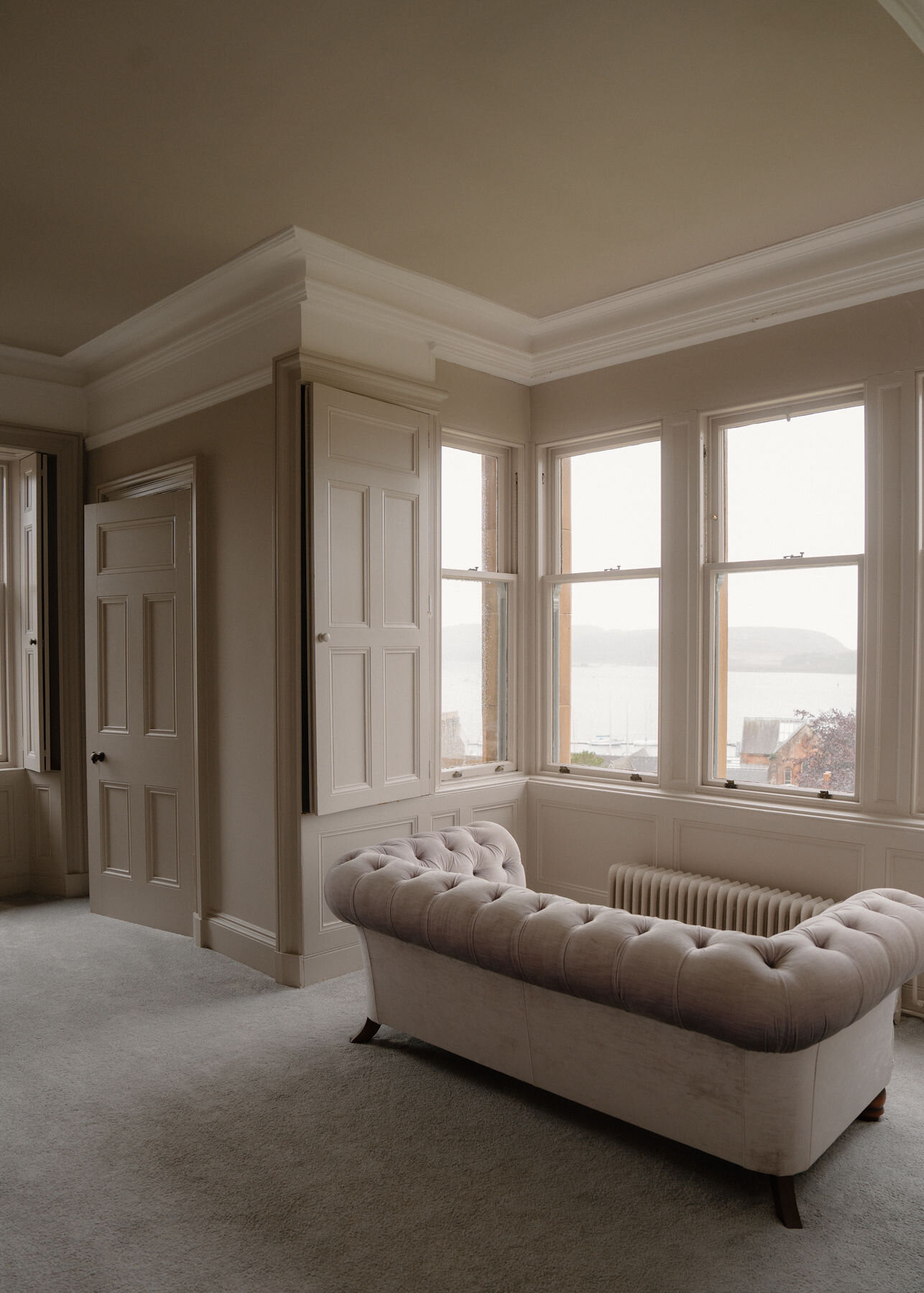 The buttoned sofa in the bay of a large bedroom, a panelled door and the sea through the windows.