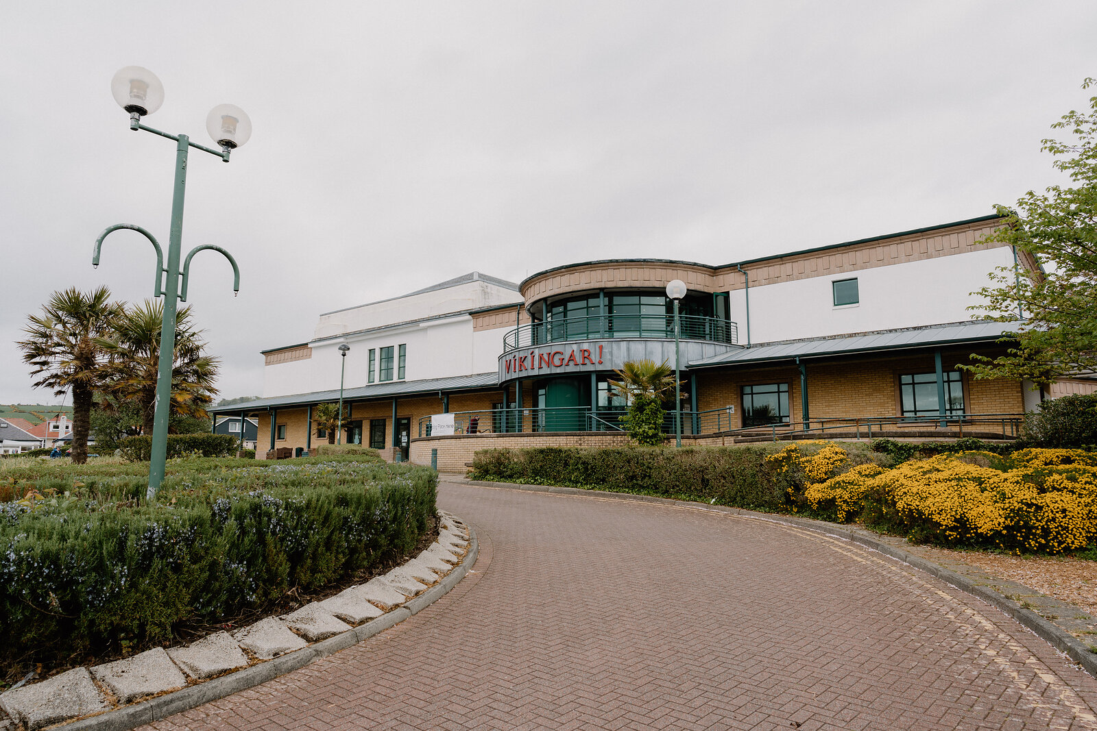 A curved building with the sign "Vikingar!" stands behind a lamp post and hedges, a gravel path curving toward the entrance.
