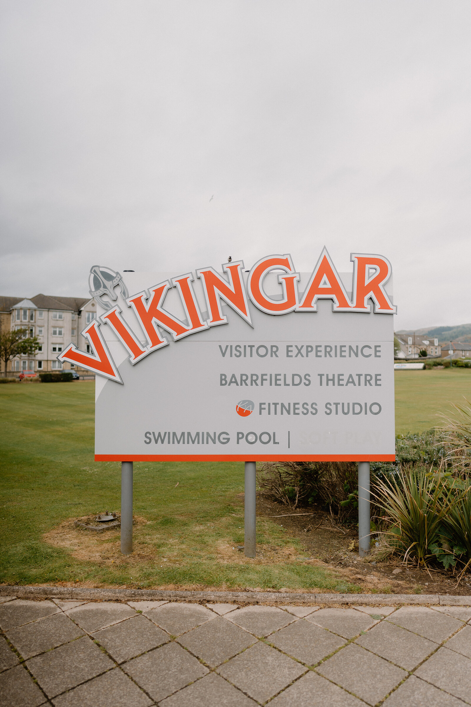 A large road sign reads "Vikingar, visitor experience, Barrfields Theatre, fitness studio, swimming pool" on a grass verge.