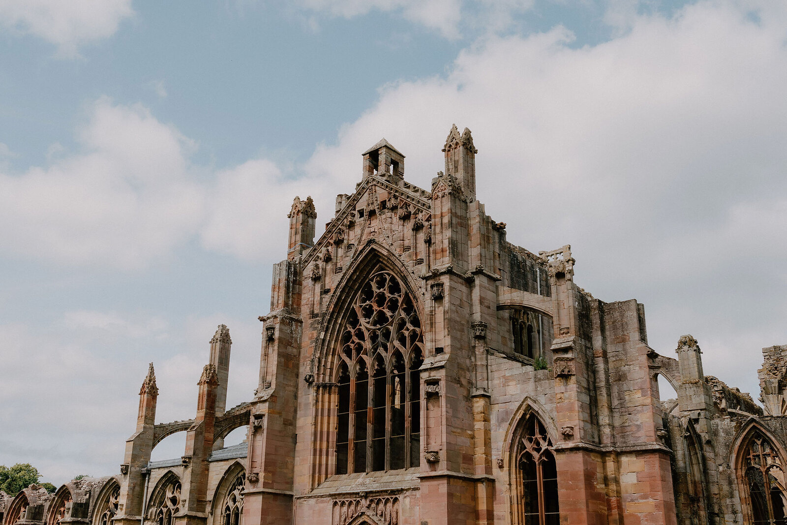 A ruined abbey's east end rises in tiers of pointed windows and pinnacles, a small bellcote crowning the gable.