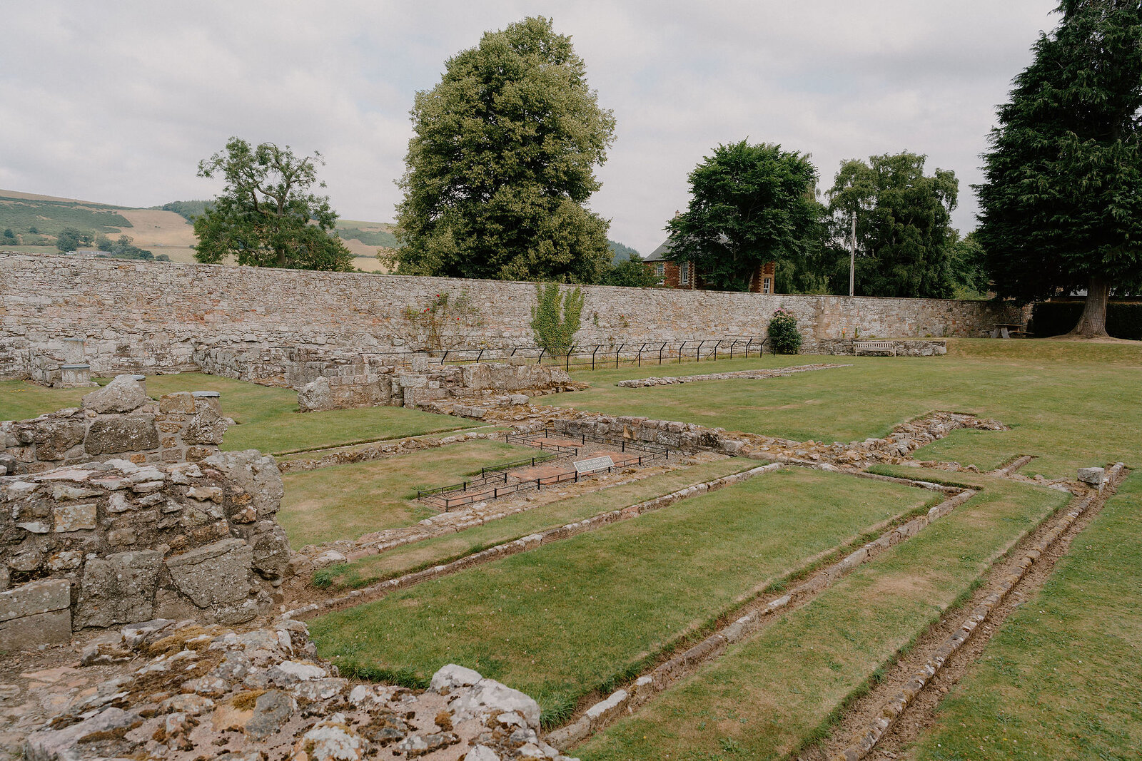 The excavated foundations of a monastic building lie within a walled lawn, low stone walls tracing out former rooms.