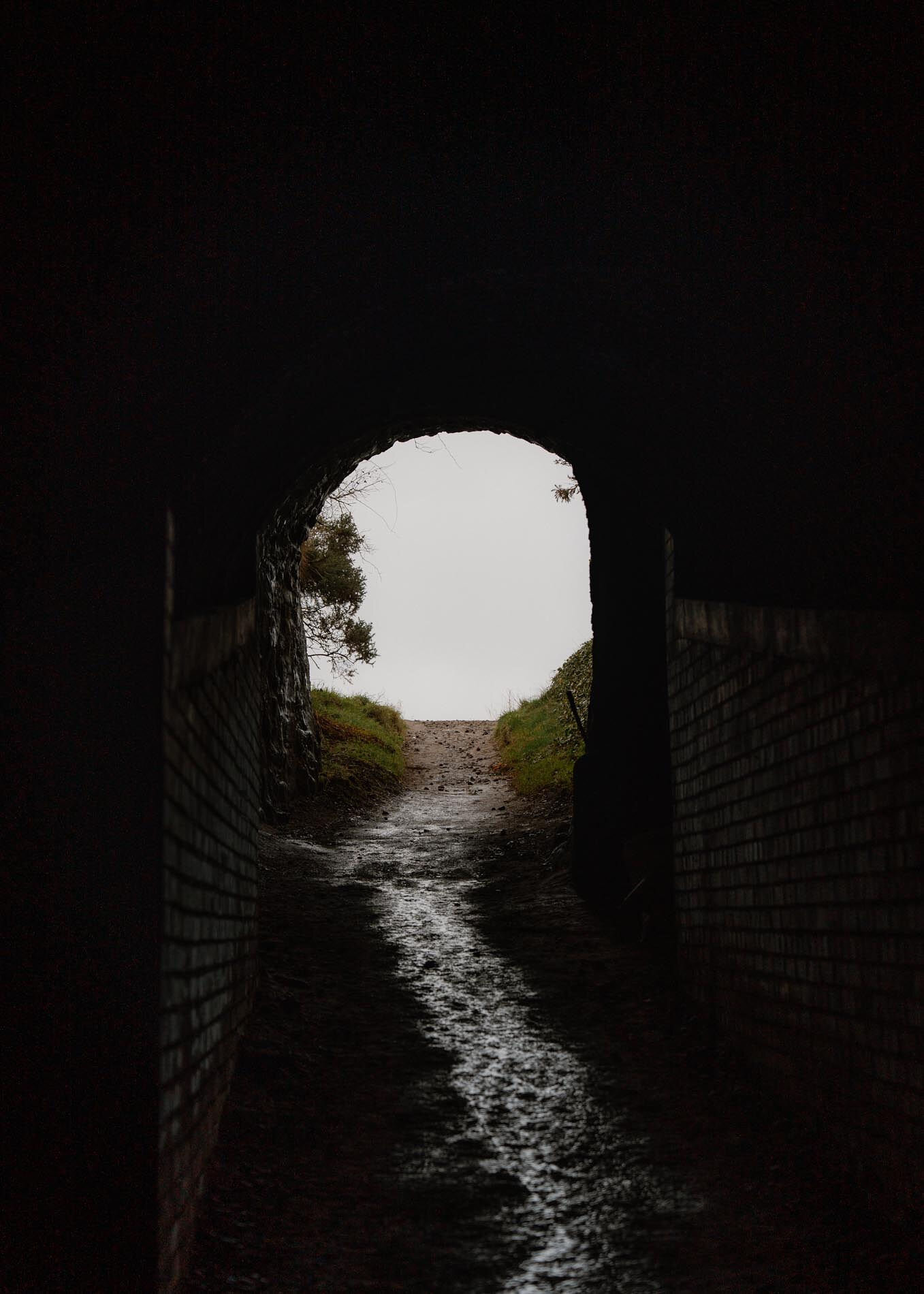 The 1752 rock-cut tunnel in near darkness, daylight at its far end and water running down the floor.