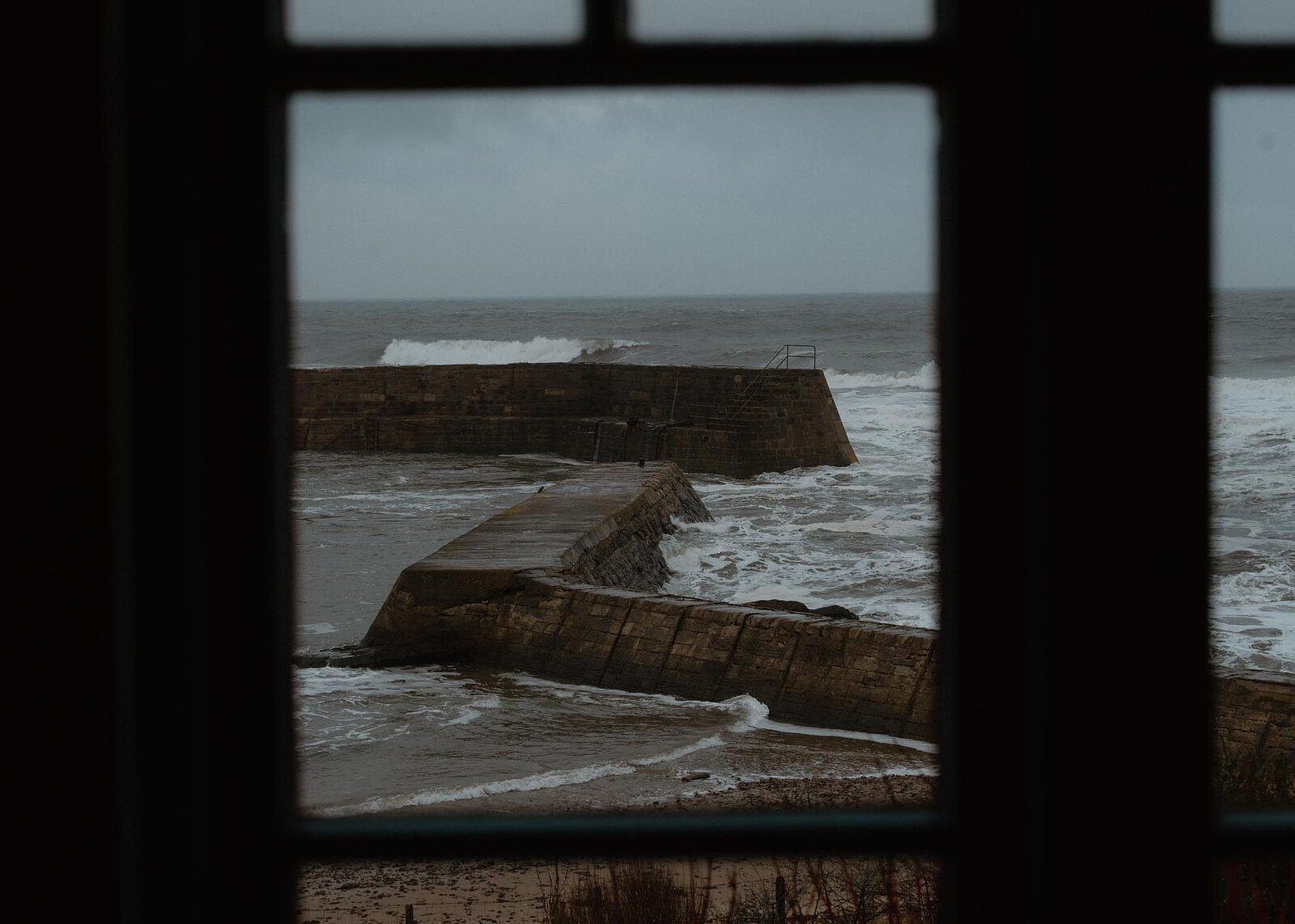 A landscape frame of the piers and breaking surf through the window's glazing bars.