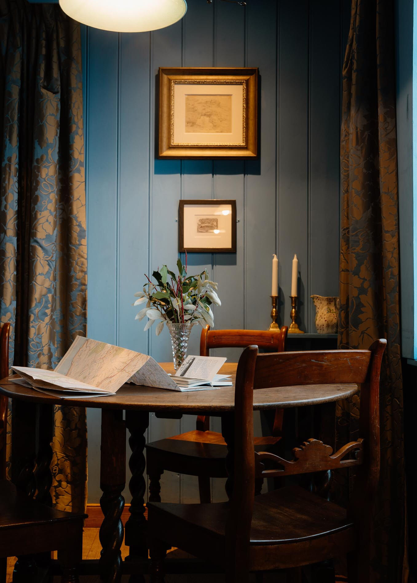 Closer on the round table with an open chart, candlesticks and a jug of flowers under the lamp.