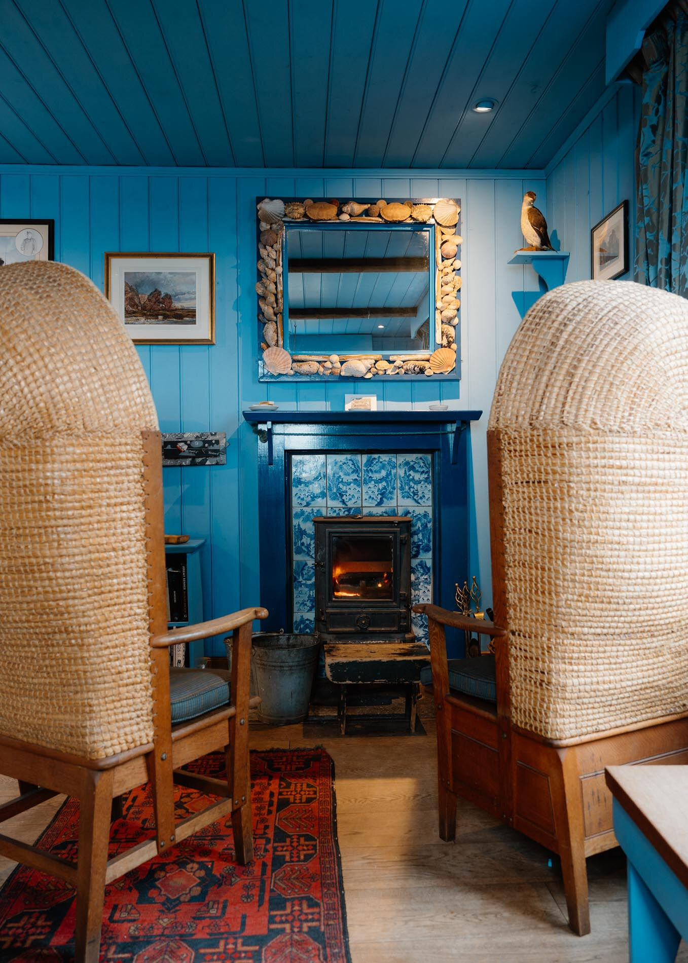 Between the straw hoods of the two Orkney chairs, the lit stove in the blue-tiled fireplace.