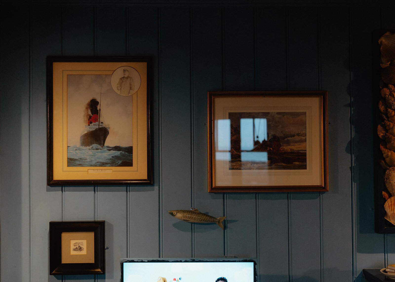 Old maritime prints on the cabin's blue boards: a liner in a gale, a stormy harbour and a carved fish.