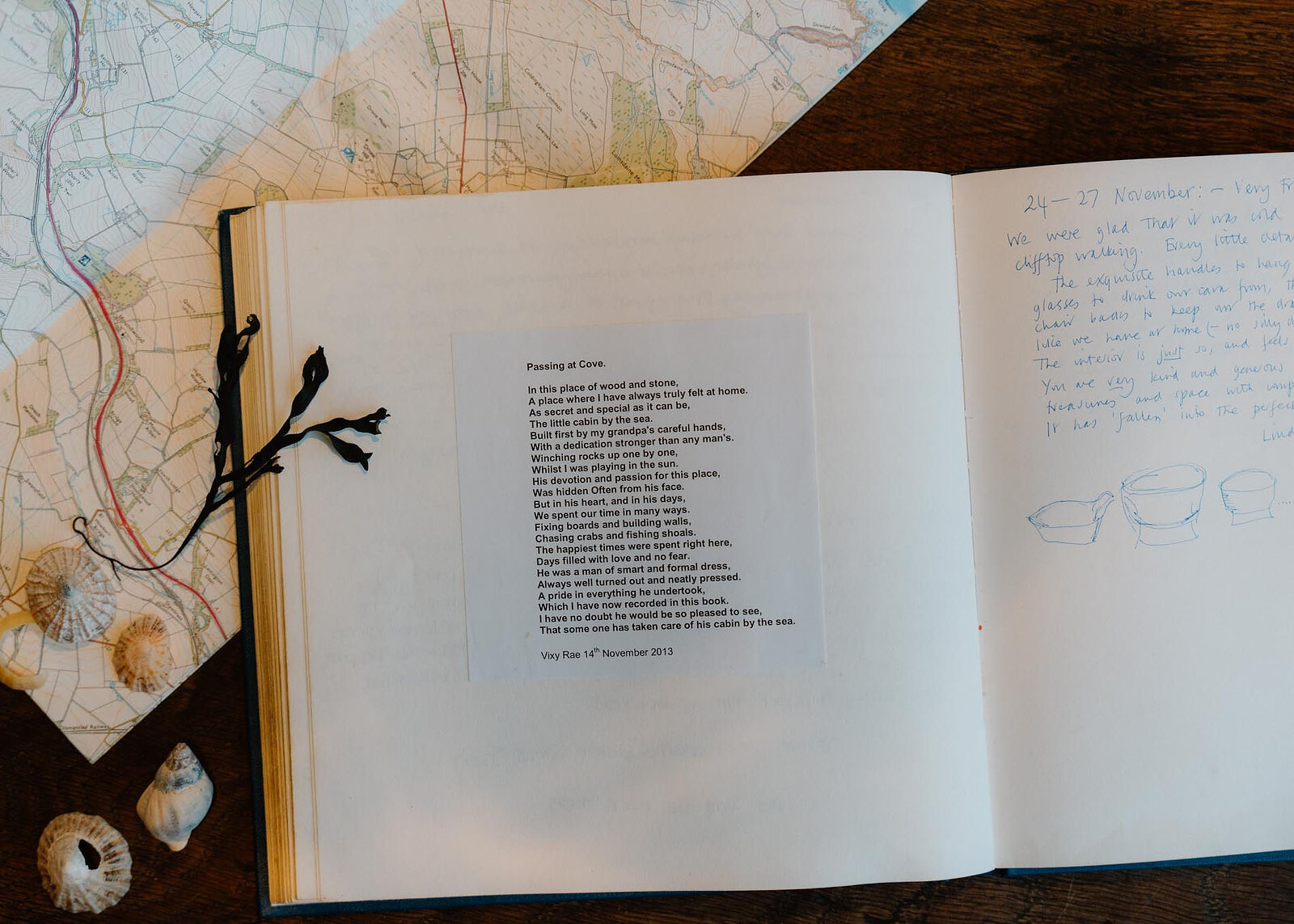 The guest book open to a poem, Passing at Cove, and handwritten notes and drawings from guests, shells on the map beside it.