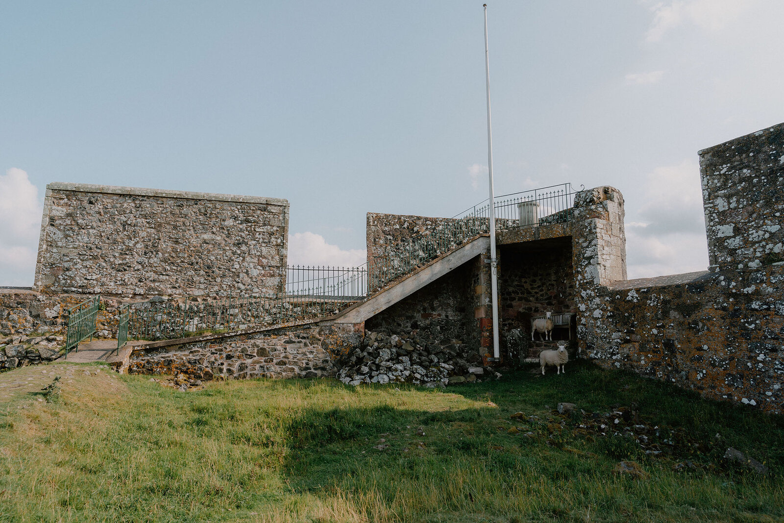 A ramped stone walkway leads up between the walls of a fort, a flagpole rising from the battlements above.