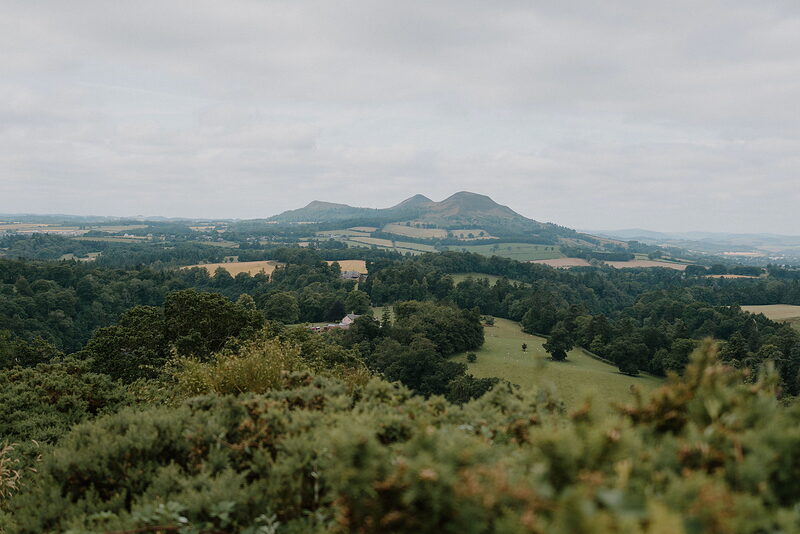 A distinctive three-peaked hill rises above farmland and hedgerows stretching into the distance.