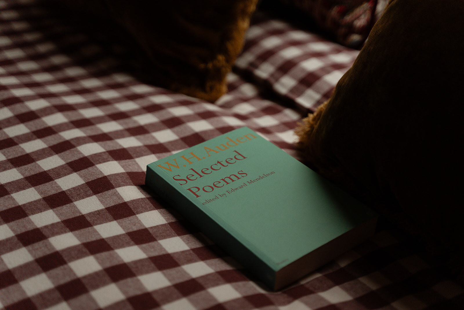 A book of selected poems lying on a red and white gingham bedspread.