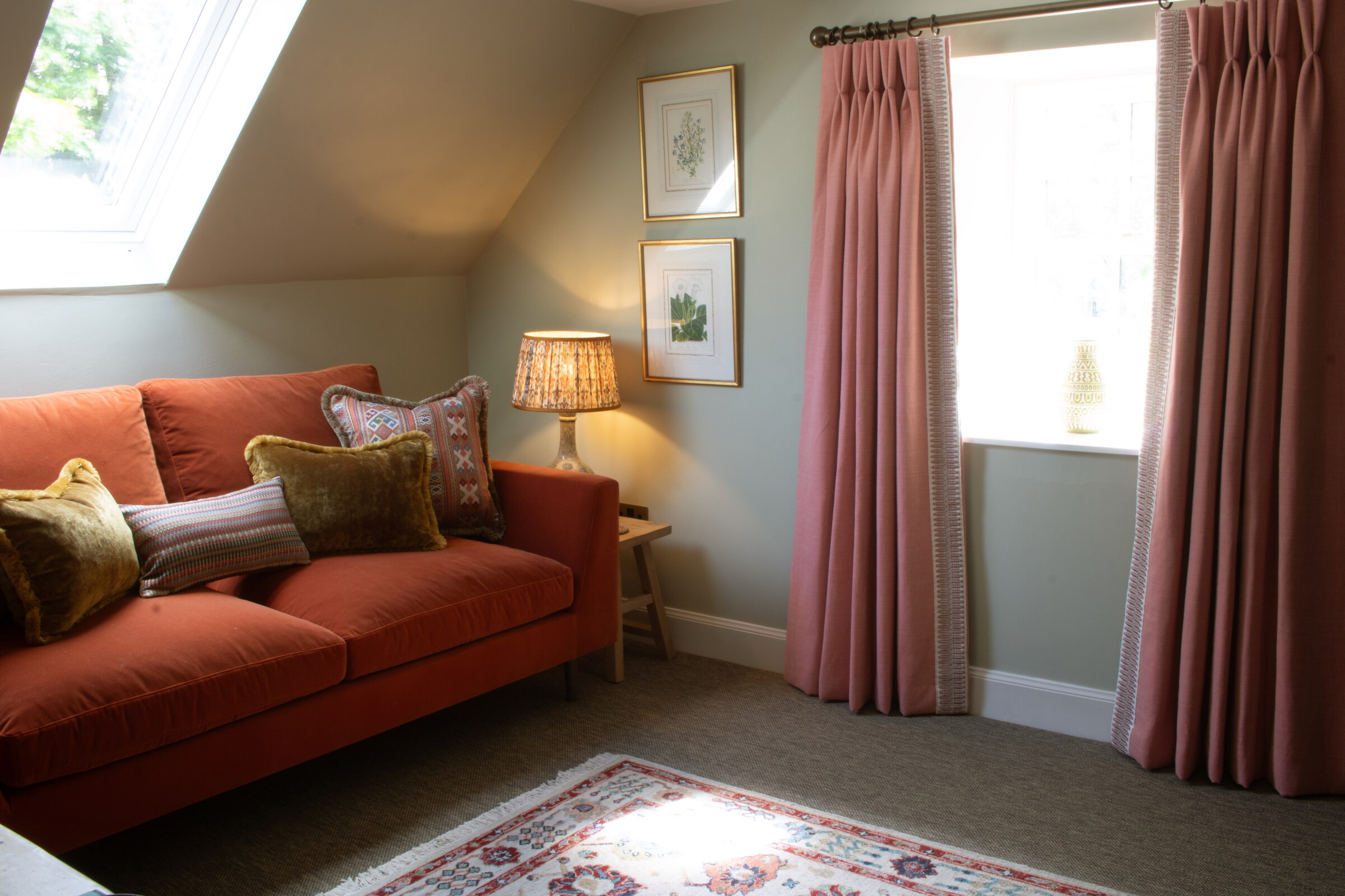 The first-floor drawing room, a rust velvet sofa below a skylight, framed botanical prints, pink curtains and a patterned rug.