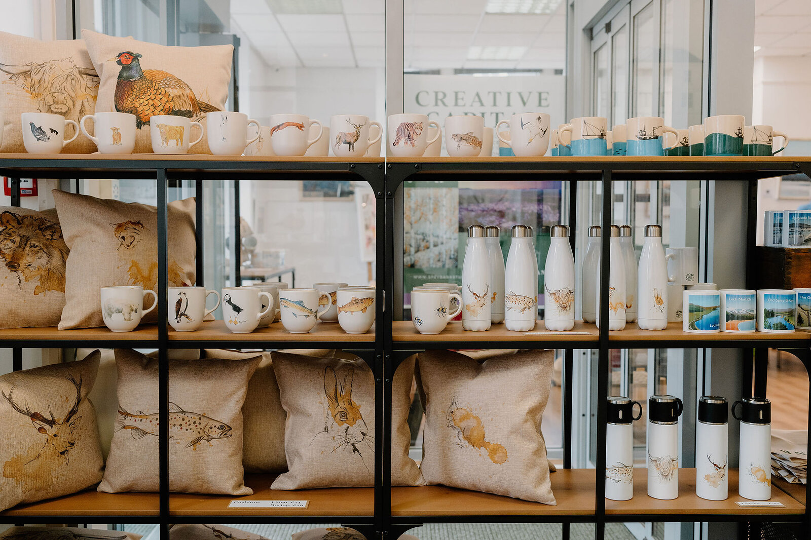 Shelves hold wildlife-themed mugs, cushions and water bottles printed with birds and animals, greeting cards and prints displayed alongside.