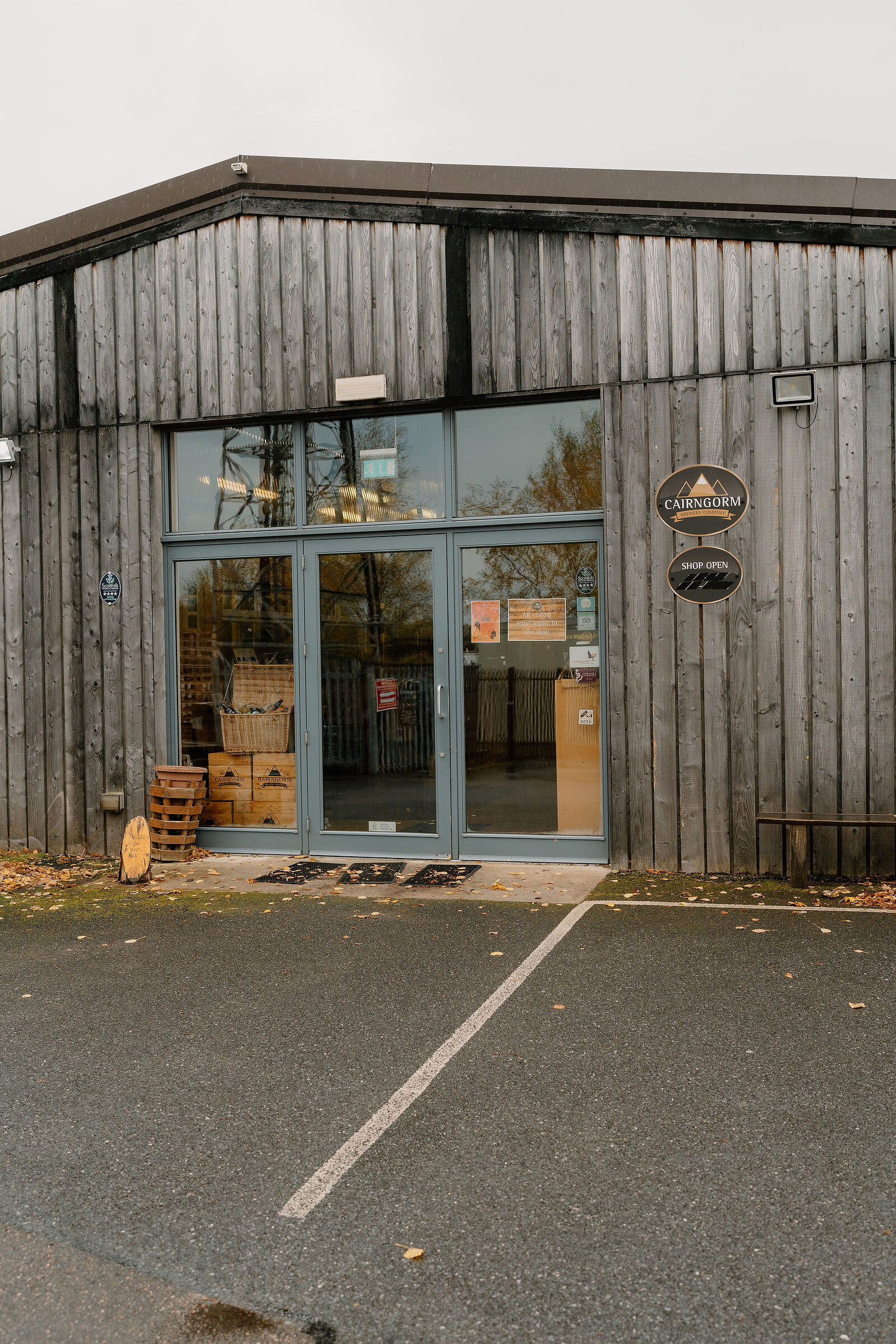 A timber-clad brewery shop entrance carries a round sign reading Cairngorm, Shop Open, crates and a barrel stacked outside the glass doors.
