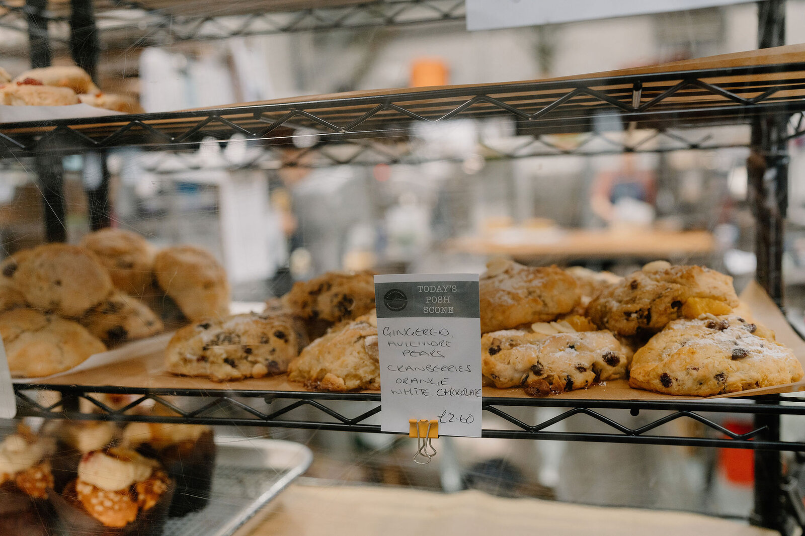A bakery display case holds cookies studded with chocolate chunks, a handwritten price sign propped among them.
