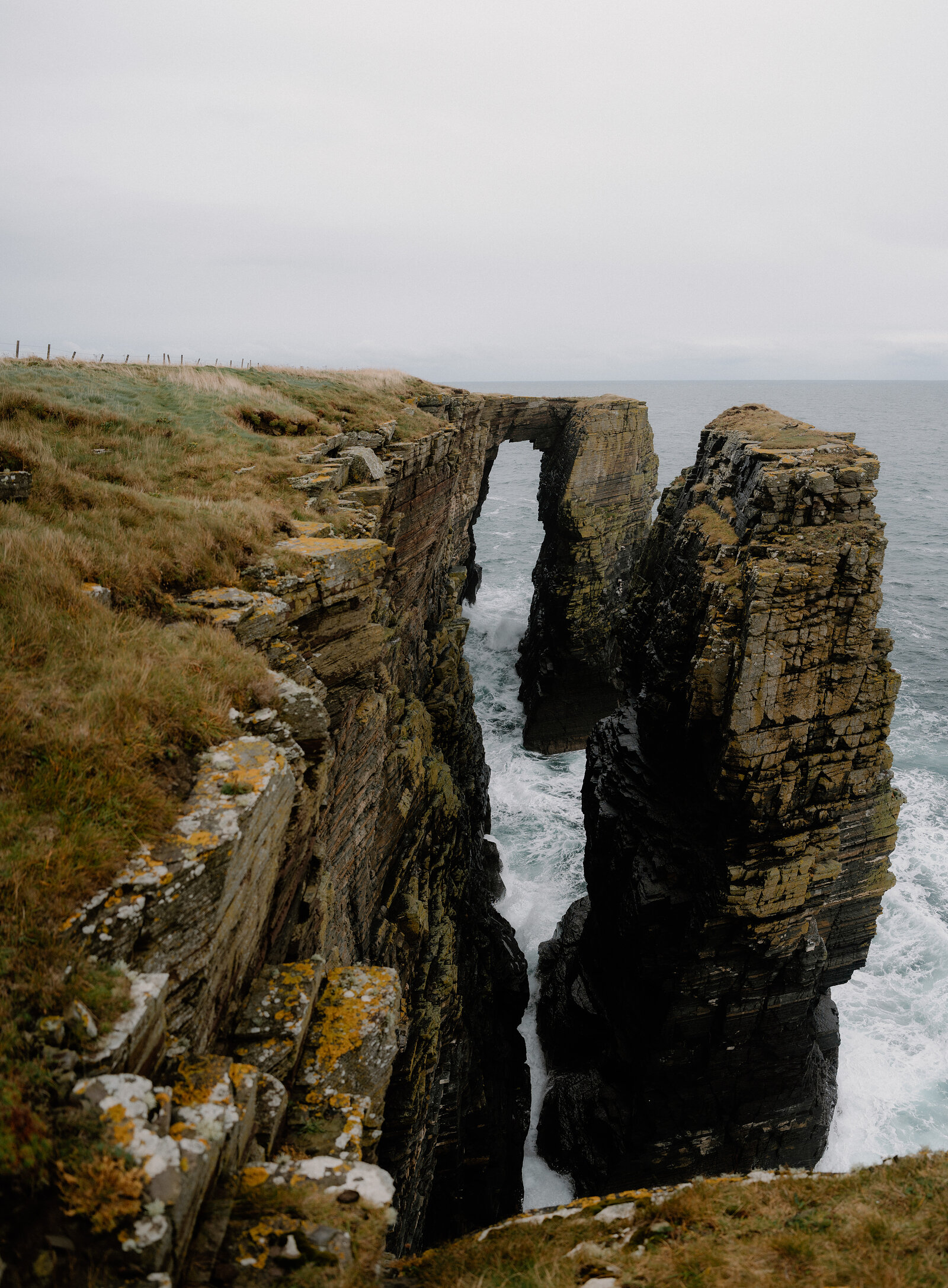 A rock arch bridges two headlands above a narrow channel, waves breaking white where the sea forces through.