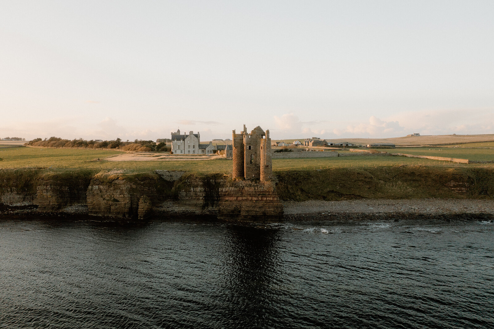 Keiss Castle on its low cliff above the sea, the white gabled Keiss House across the field behind it.