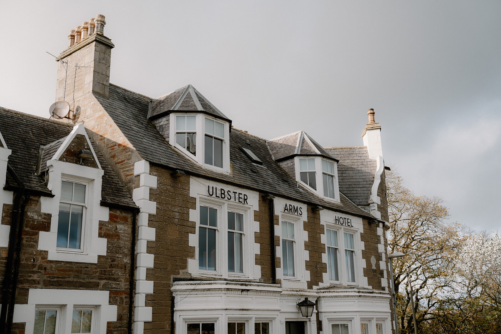 A stone hotel with two gabled dormer windows and tall chimneys is signed "ULBSTER ARMS HOTEL" along its roofline.