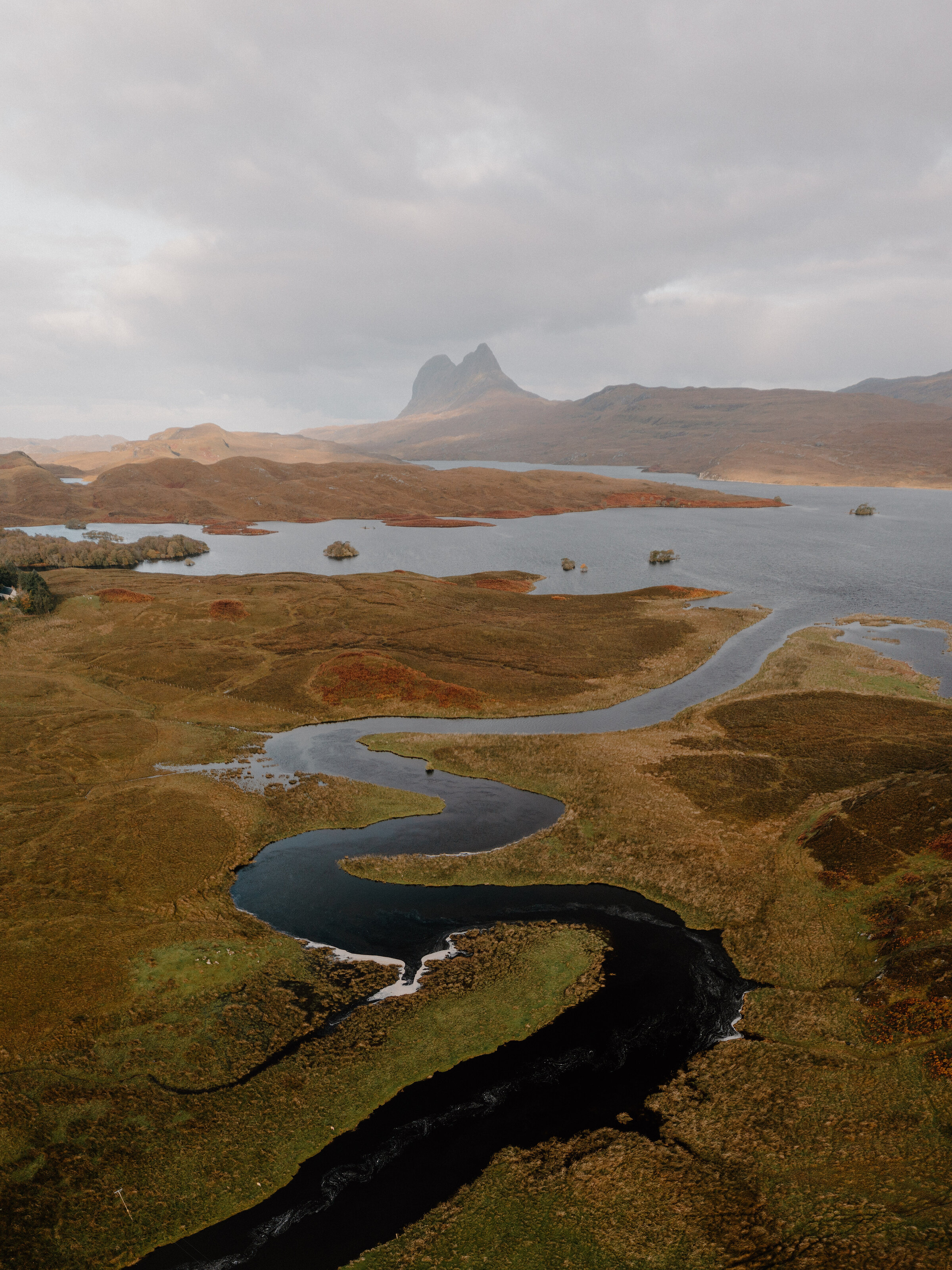A river winding across the Assynt moorland to a loch, under a jagged peak in the mist.