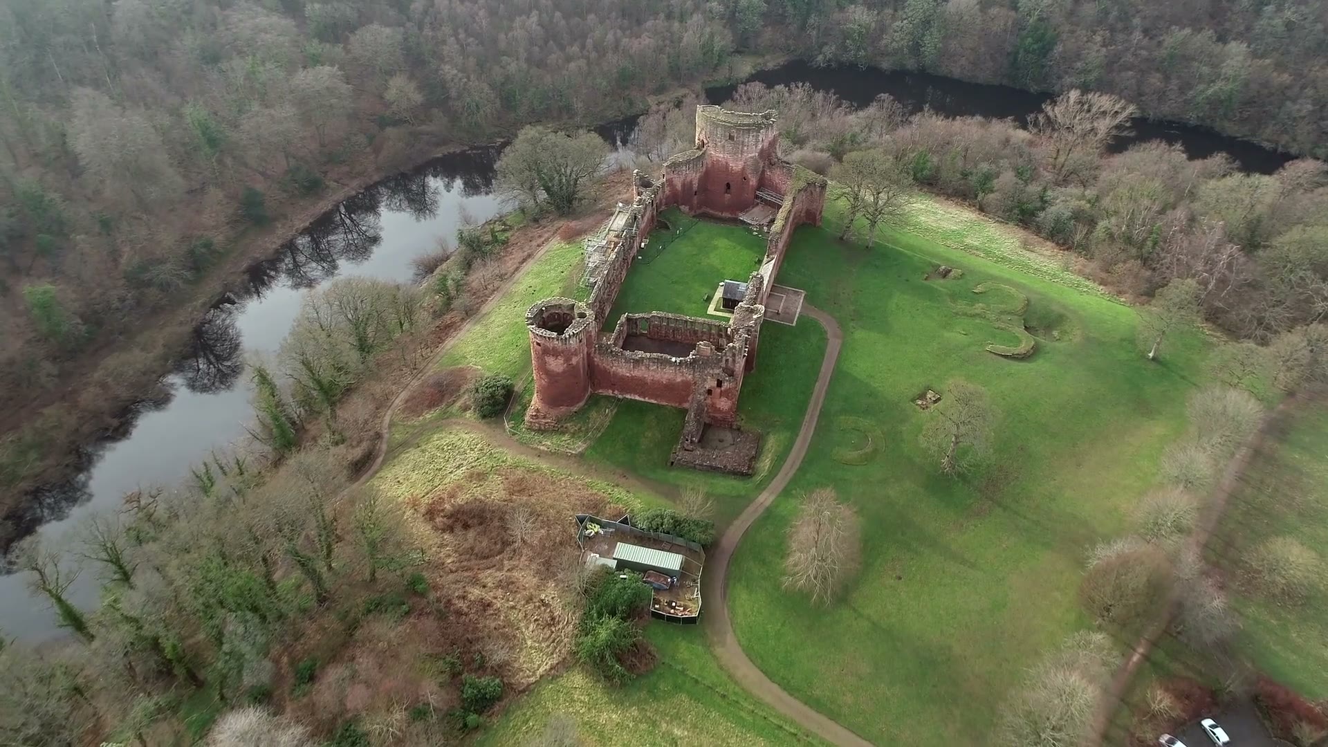 Bothwell Castle from the air on its green ground above a bend of the River Clyde, the woods dark along both banks.