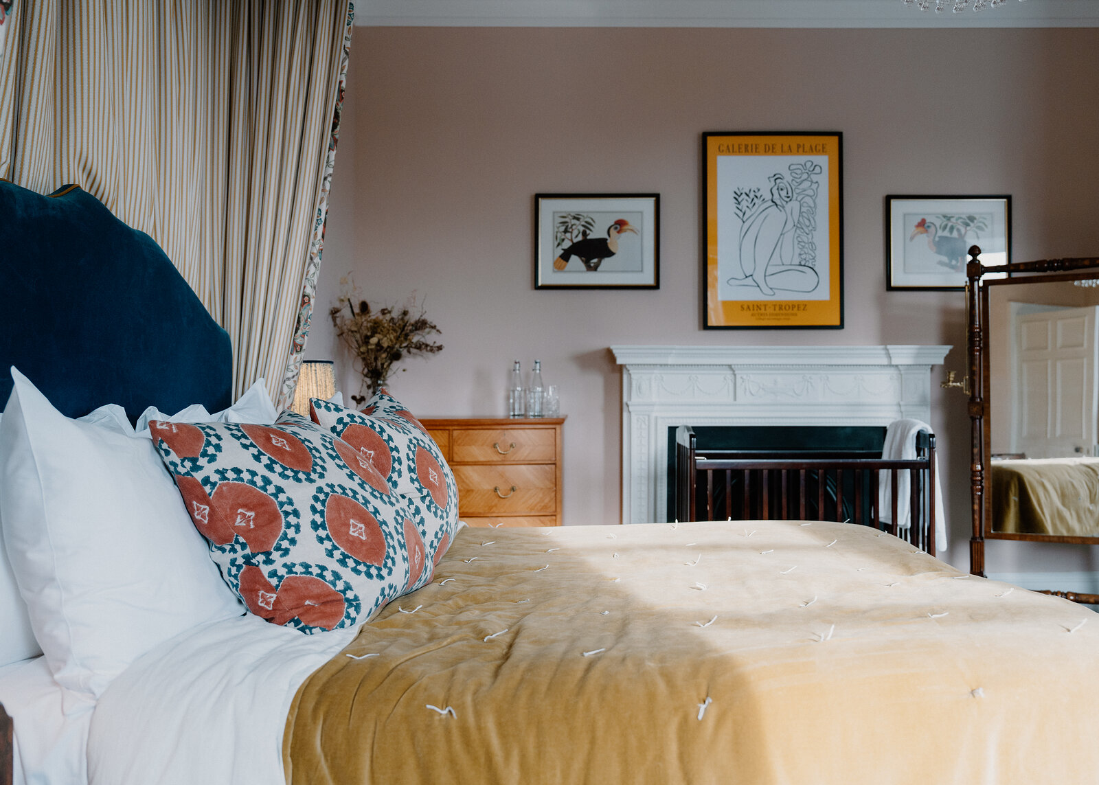 A Cromlix bedroom in soft pink, the bed made up in white and gold beneath framed prints and a white marble fireplace