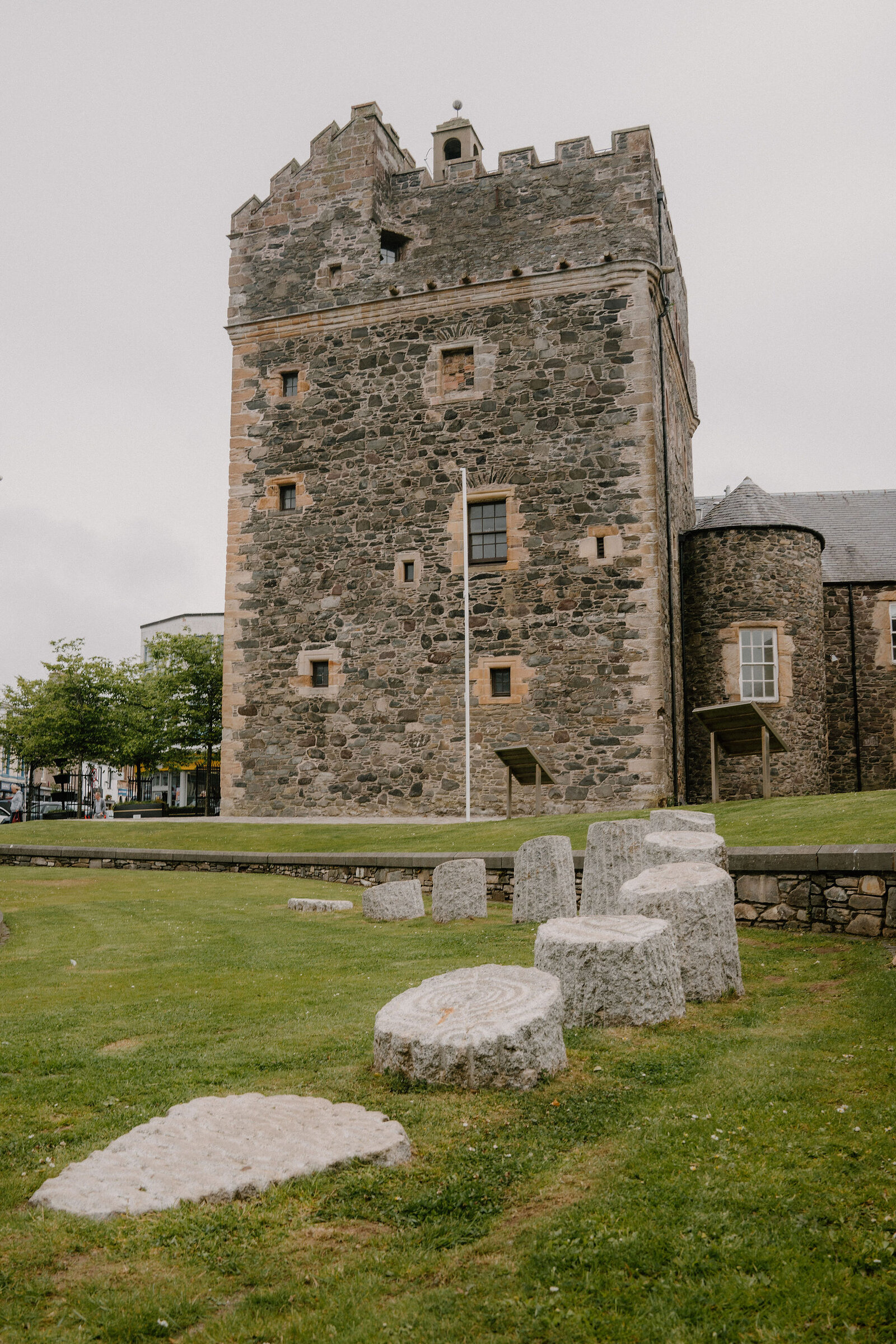 A stone tower keep with battlements stands behind a lawn scattered with carved stone artefacts.