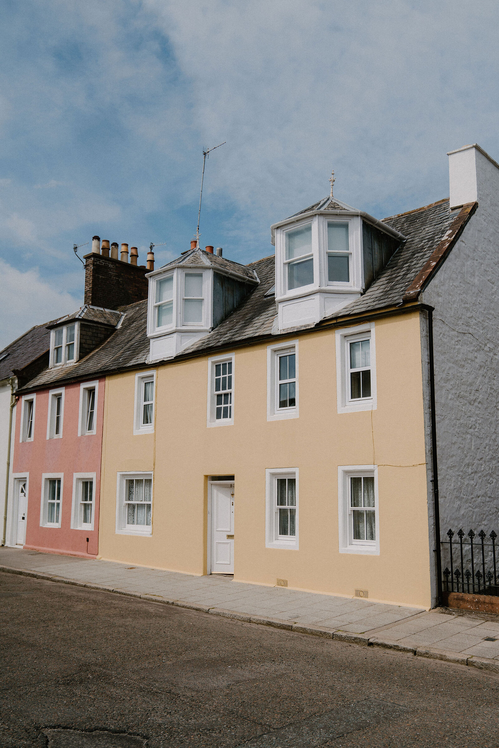 A row of pastel-painted terraced houses with dormer bay windows and chimney pots lines a quiet street.