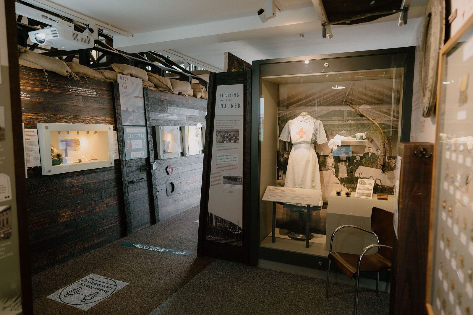 A museum display case holds a First World War nurse's uniform on a mannequin beside information panels and a folded chair.