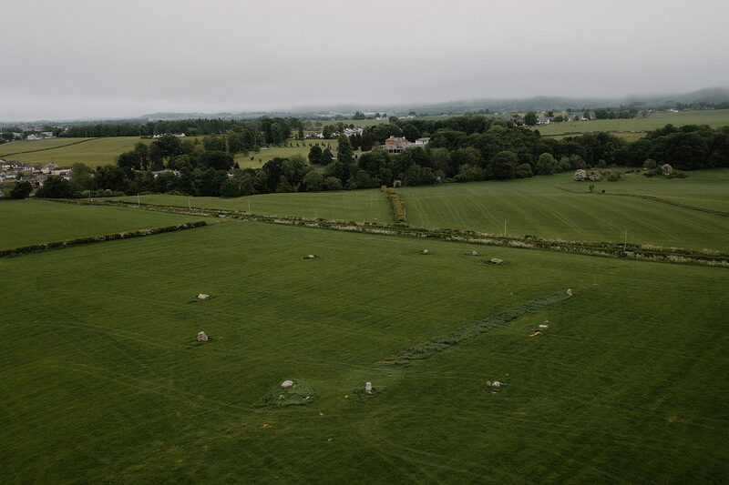 An aerial view shows farmland scarred with parallel trenches and heaped soil, a distant house and trees on the horizon.
