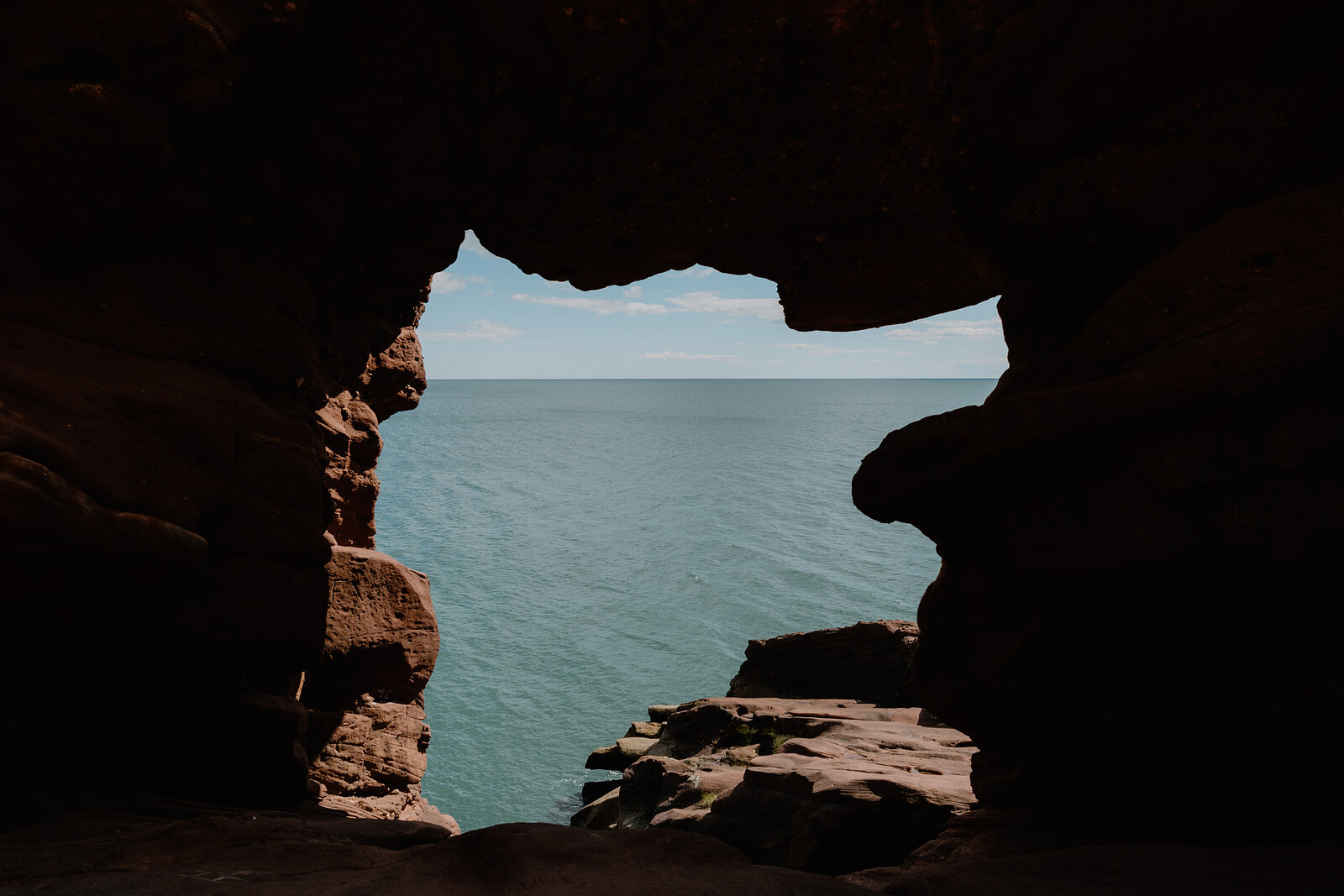A dark rock opening frames a view of open sea, layered sandstone walls closing in on either side.