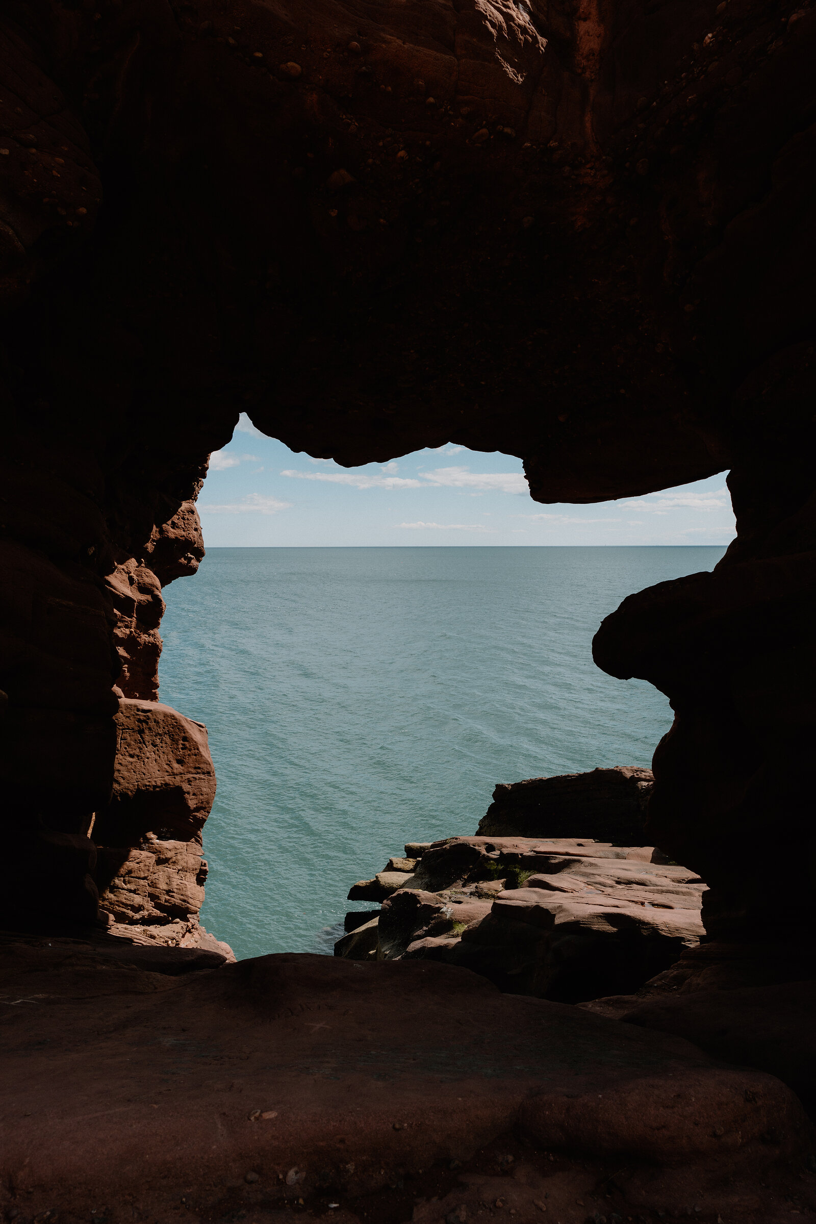 A dark rock opening frames a bright view of open sea, sandstone walls closing around the gap.