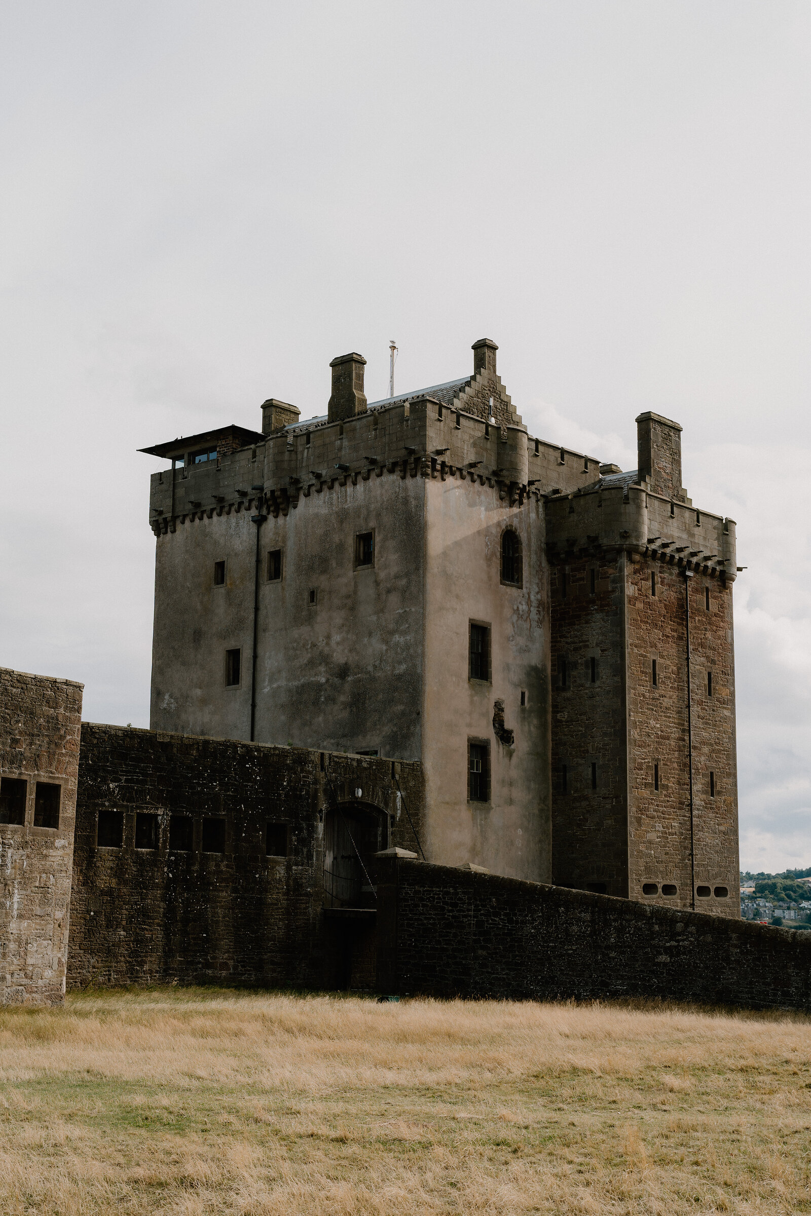 A rendered stone tower castle with battlements and corbelled turrets rises behind a fortified curtain wall.