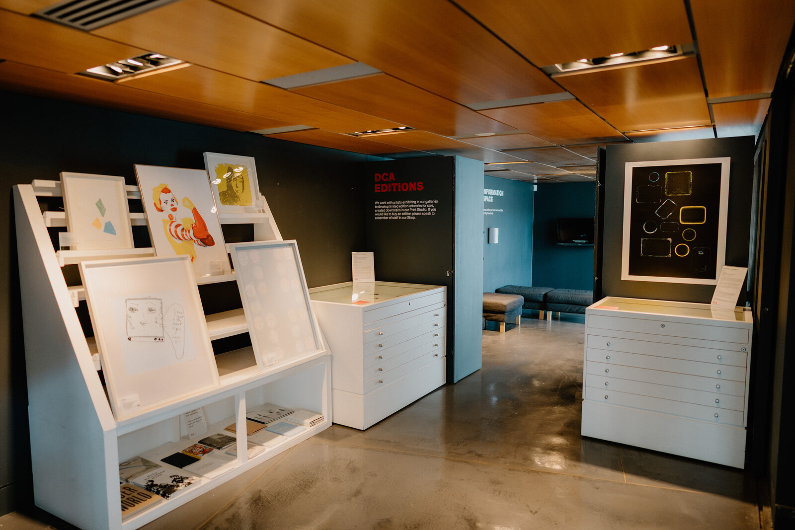 A gallery room labelled "Editions" displays framed prints on white plan chests and a wooden easel beneath a timber ceiling.