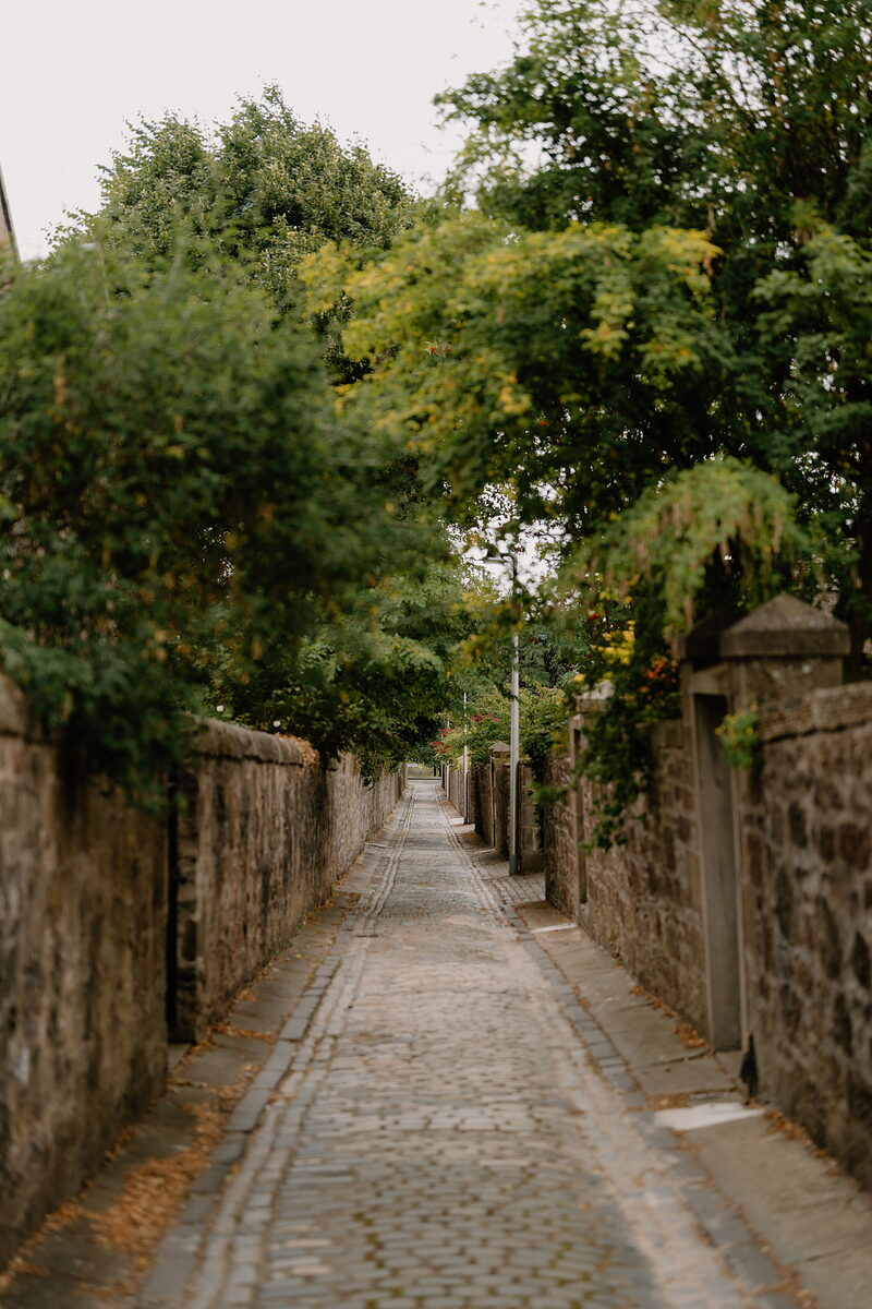A narrow cobbled lane climbs between stone walls, trees with early autumn colour arching overhead.