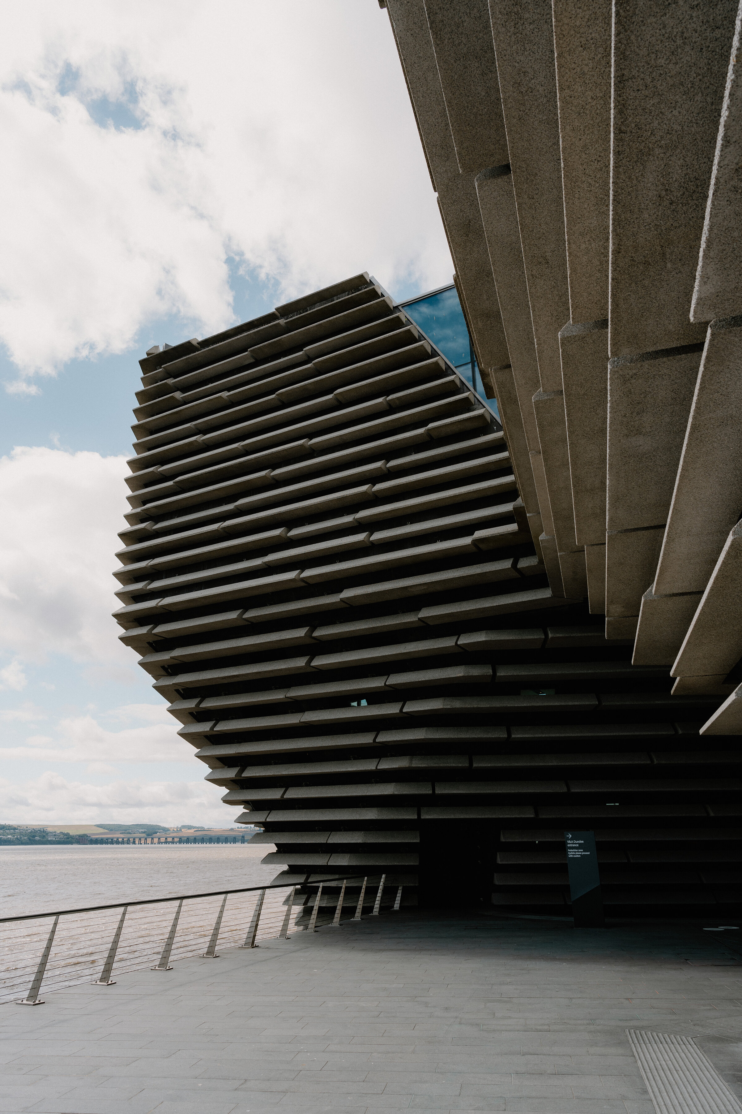 V&A Dundee's layered walls curving down to the Tay, with the hills across the water.