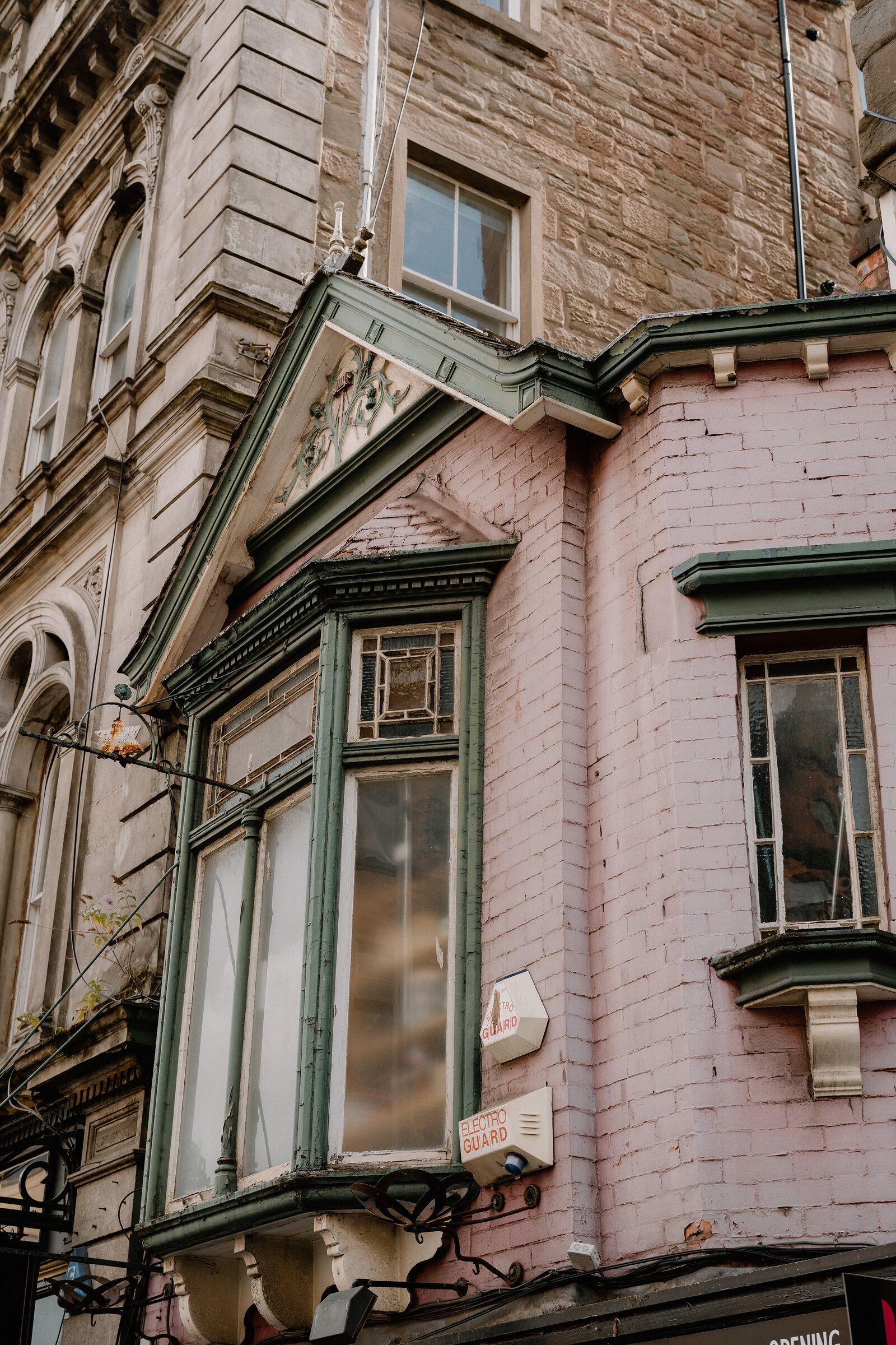 A pink Victorian building with an ornate green-trimmed gable and bay window rises beside sandstone tenements.