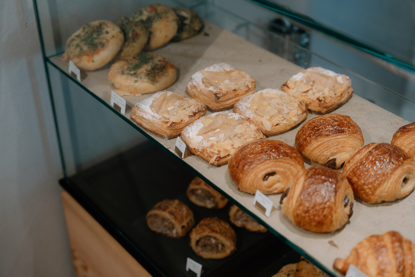 Rows of pastries fill a glass display case, including herb-topped rolls, meringue-capped buns, pains au chocolat and croissants.